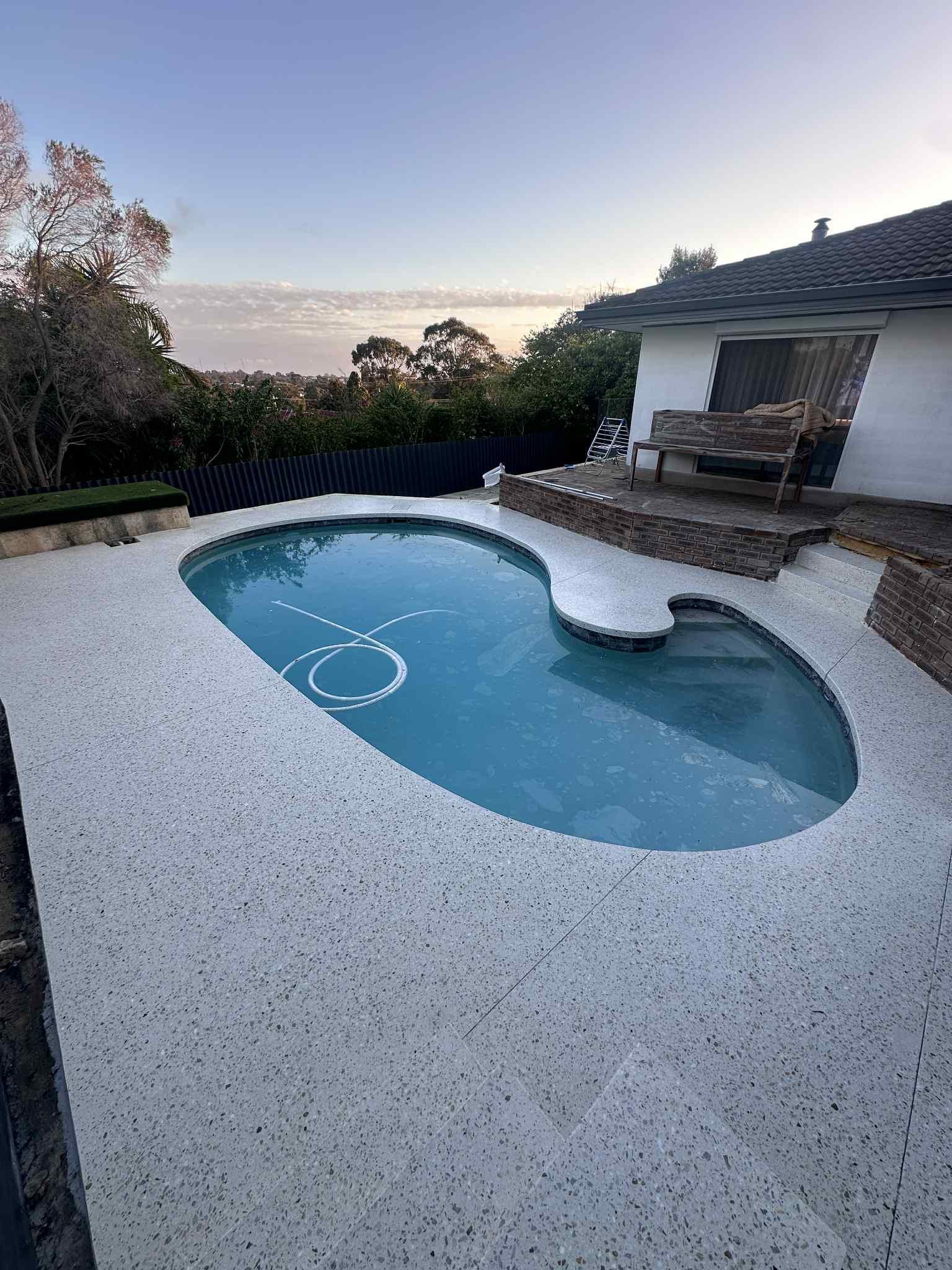 Swimming pool with blue water and white speckled honed concrete pool deck, overlooking a scenic view.