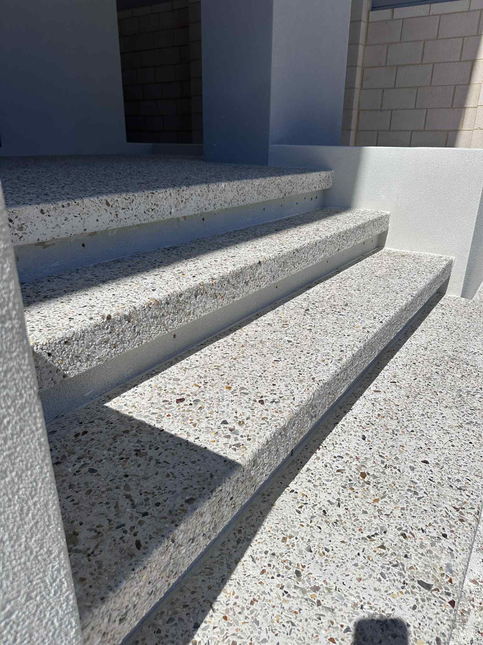 Concrete stairs with speckled aggregate, leading up to a building entrance in sunlight.