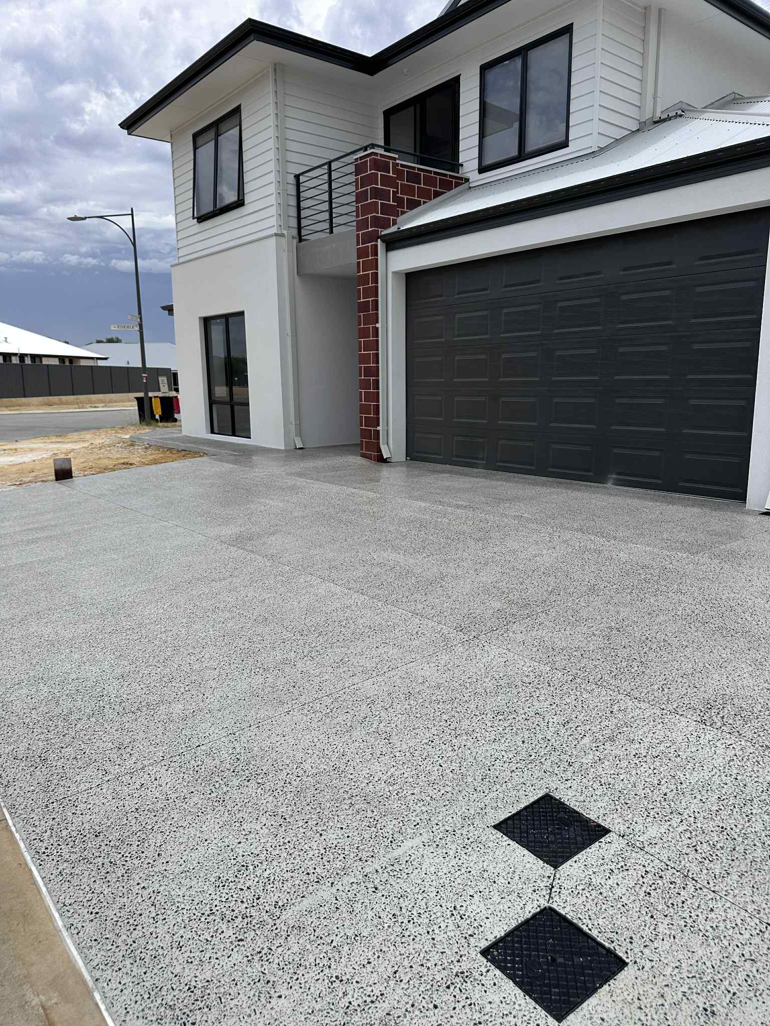 White two-story house with a speckled aggregate concrete driveway and black garage door.