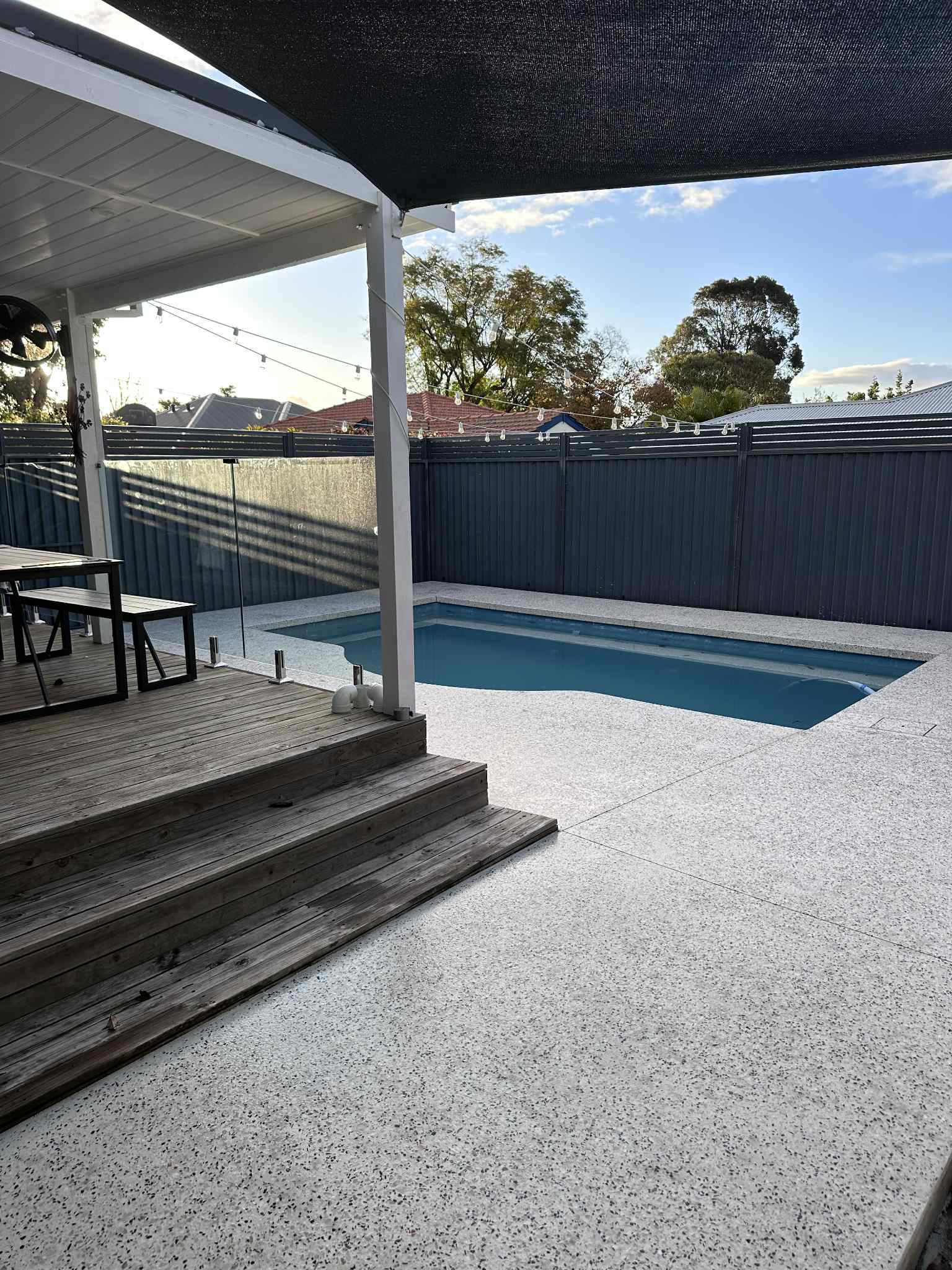 Honed concrete pool surrounds with decking and glass pool fence with gazebo