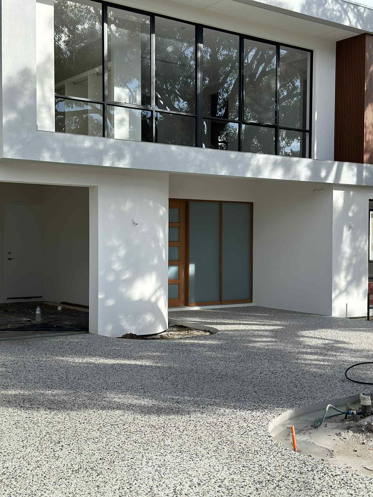 Modern white house with large glass windows and gravel driveway.