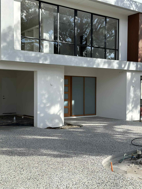 Modern white house with large glass windows and gravel driveway.