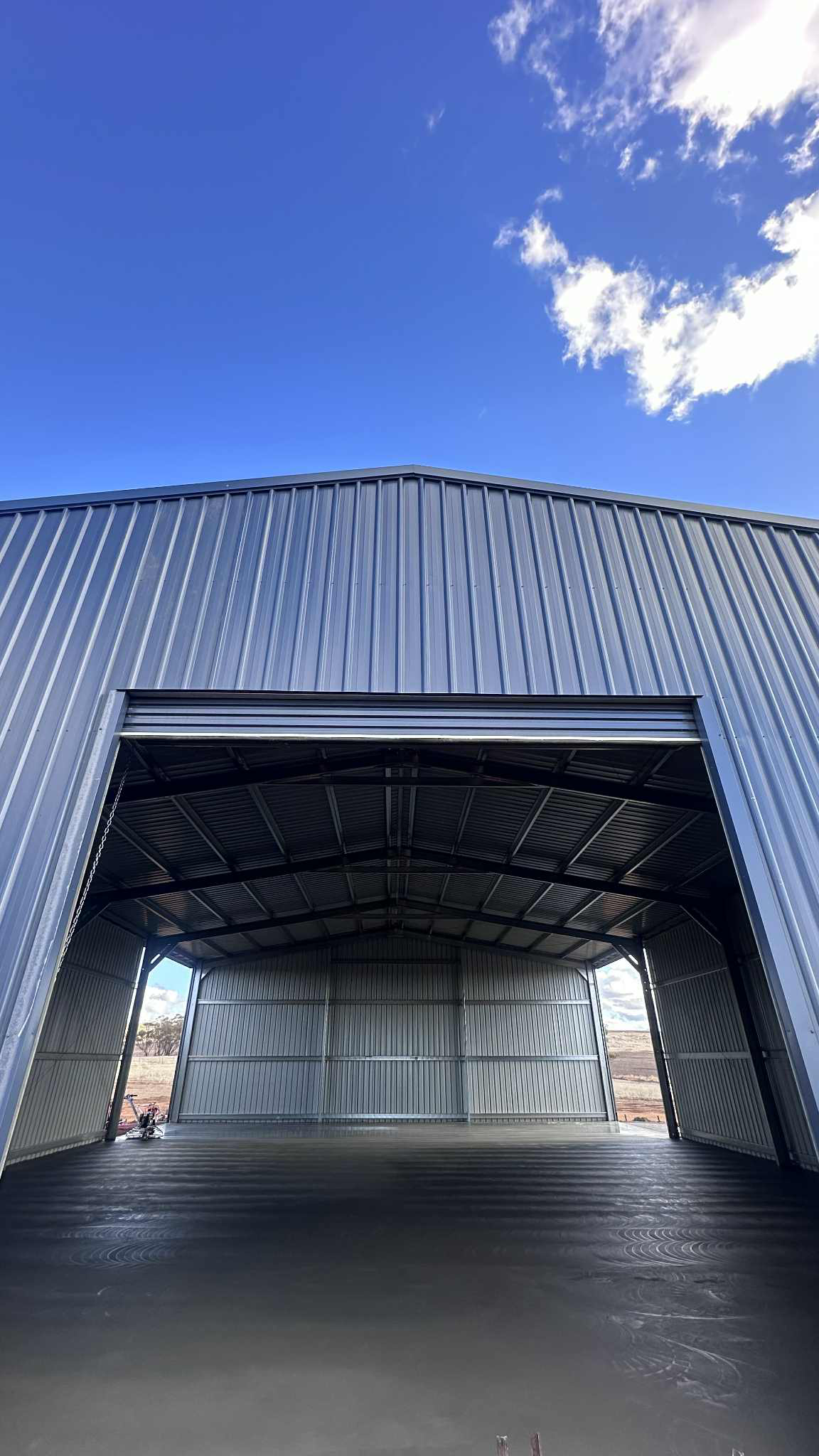 Large shed with open roller door, new concrete shed slab and concrete trowel machine