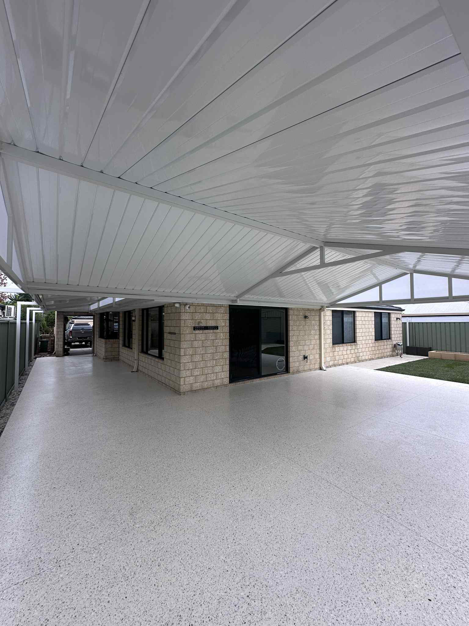 Covered outdoor patio with white ceiling and honed concrete floor by Woodlands Construction extending from a brick house.