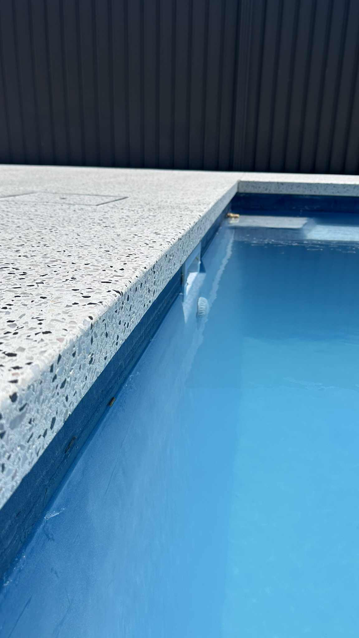 Close up of honed concrete pool noising over hanging pool edge with water in pool