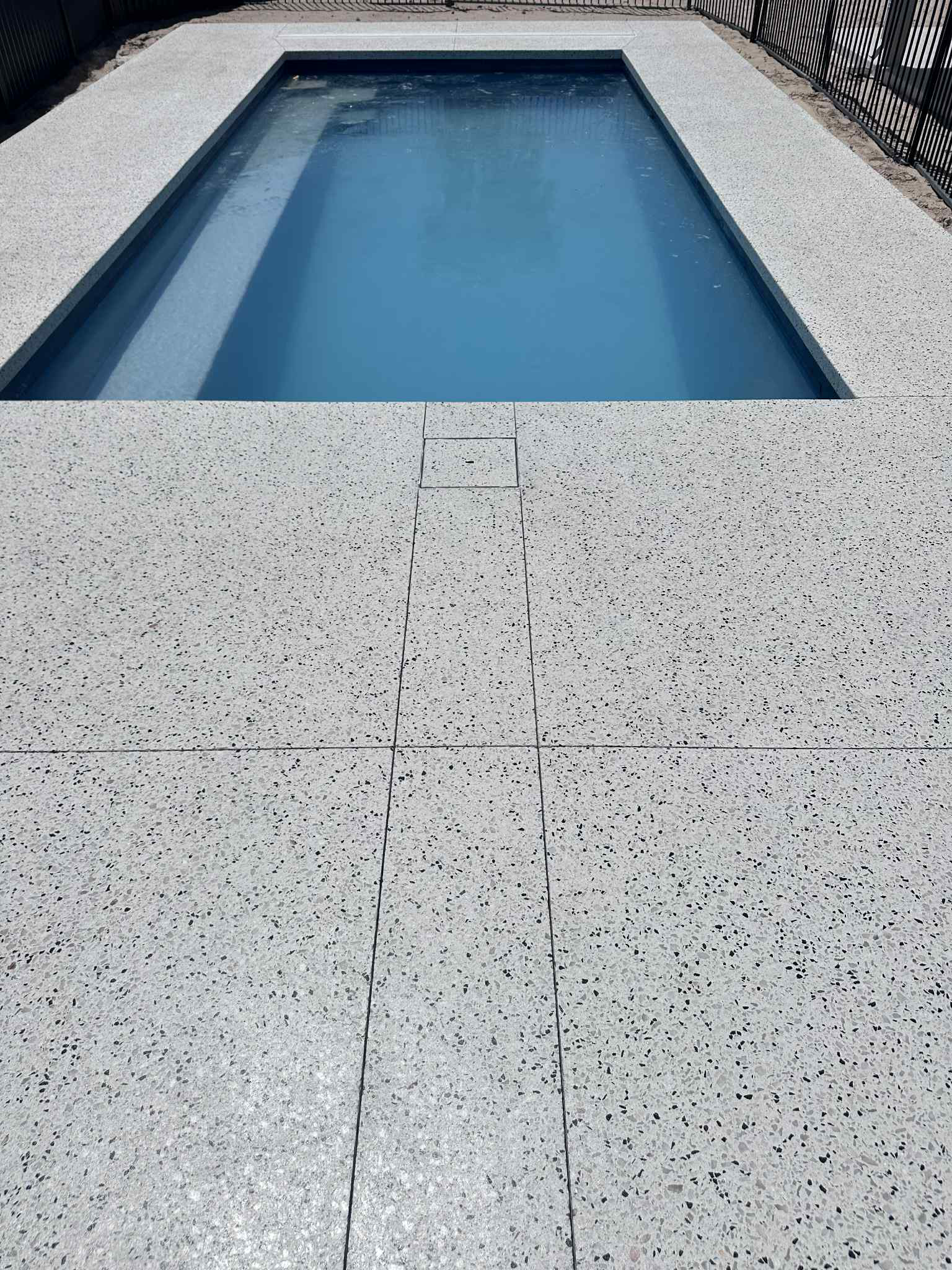 Honed concrete pool area with custom skimmer box lid and blue water