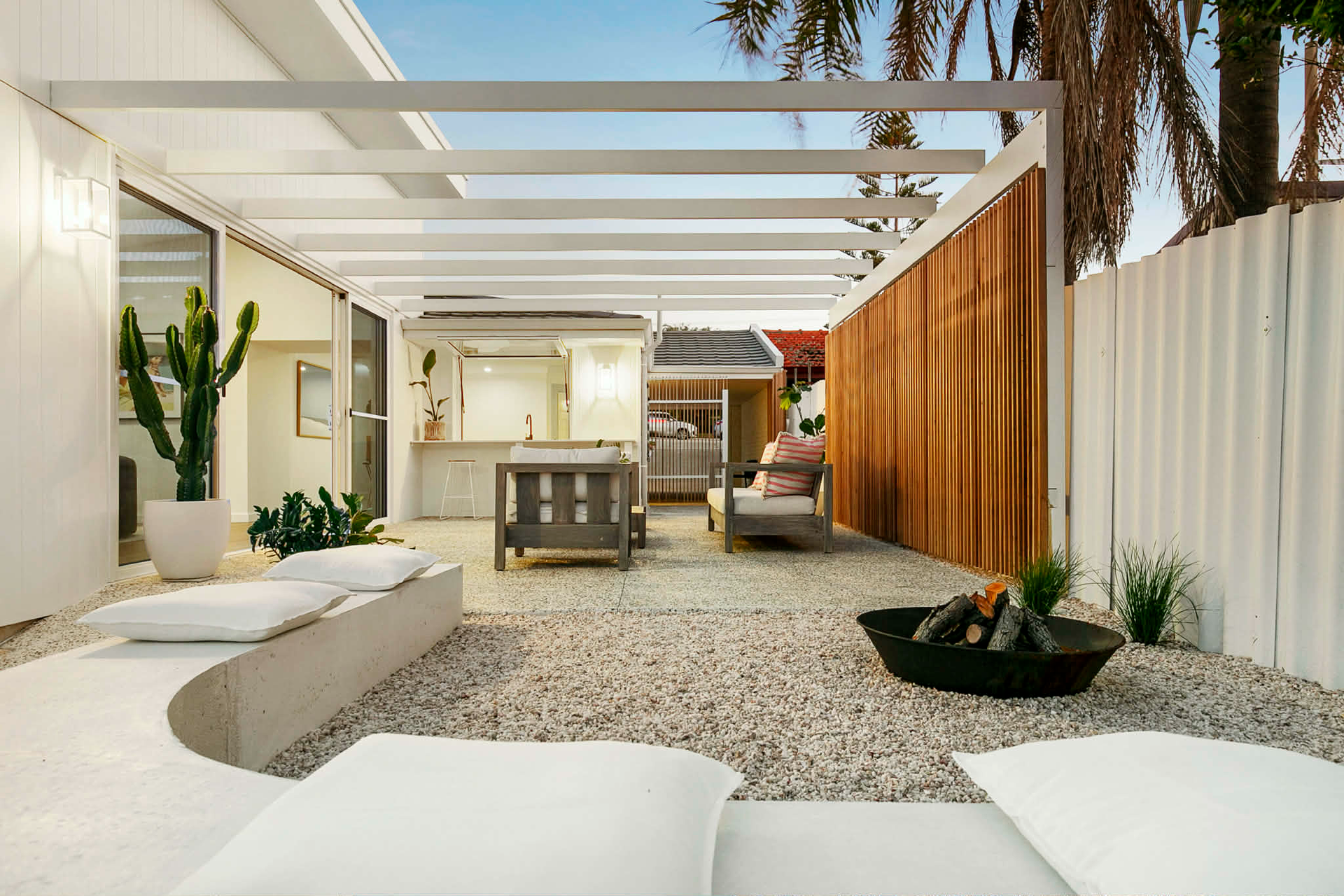 Modern outdoor patio with a white pergola, gravel flooring and a architectural concrete bench seat,