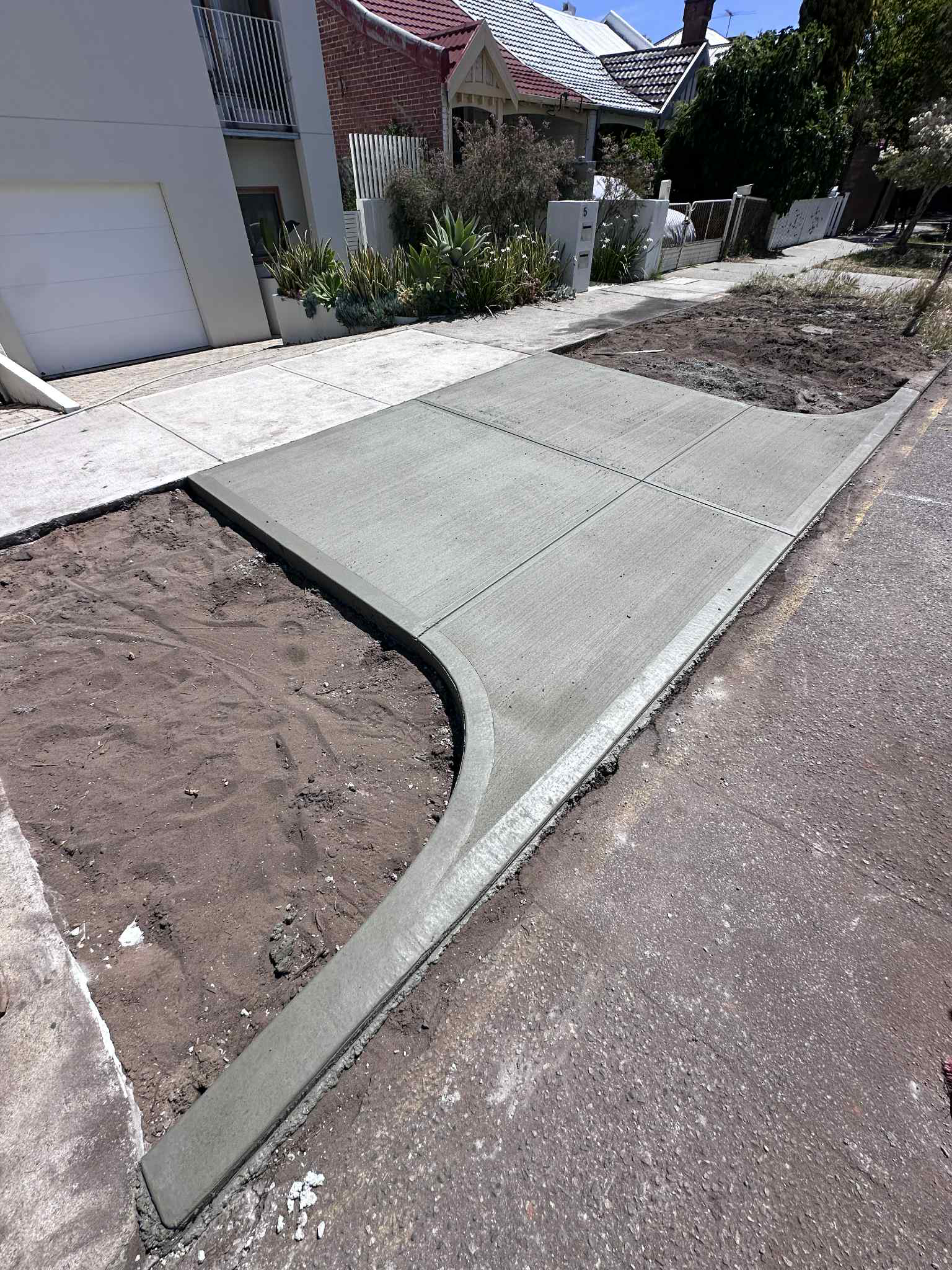 Freshly poured concrete driveway section beside a street, with an unfinished area of soil.