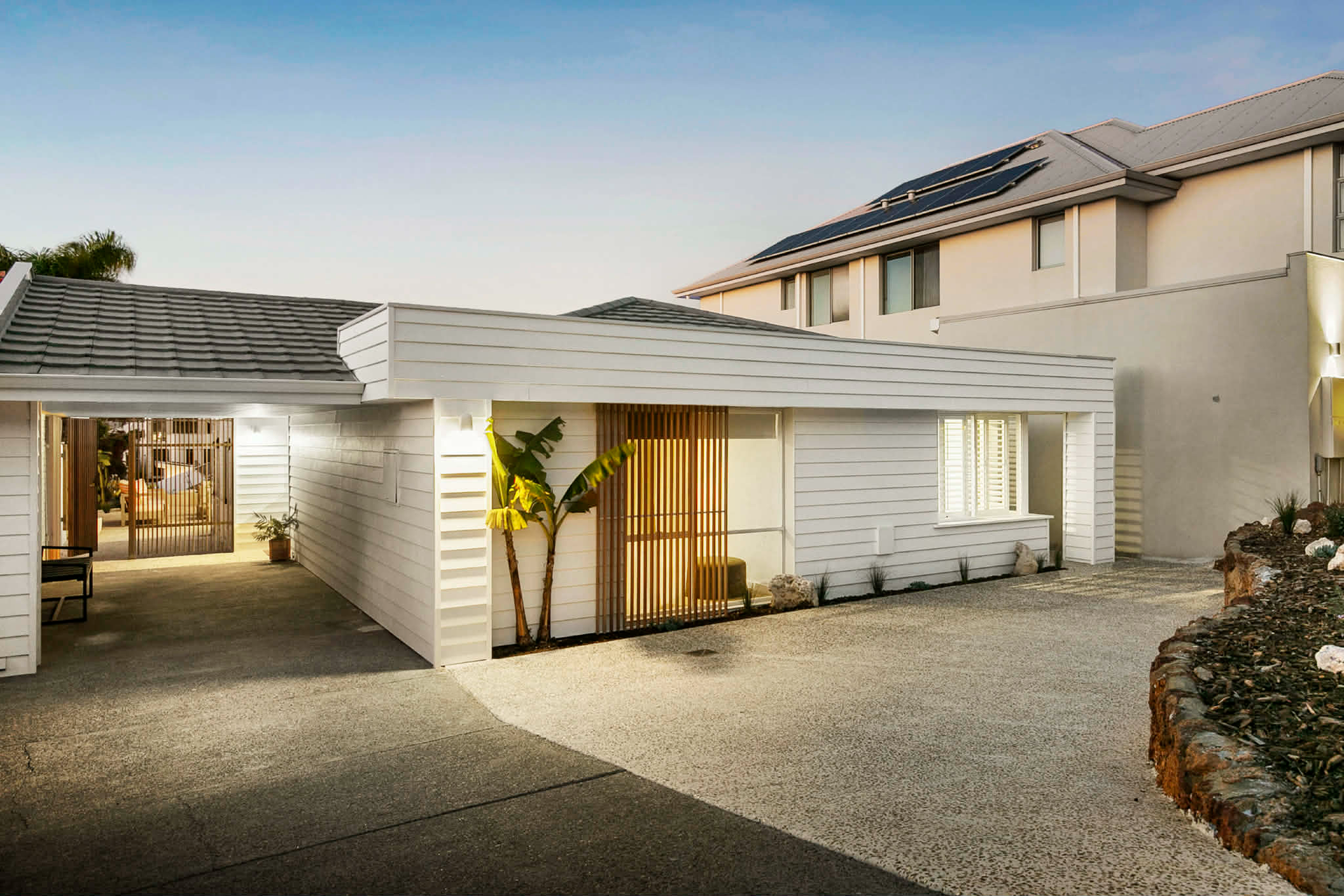 White cottage-style building with carport and exposed aggregate driveway. Palm trees and other lands