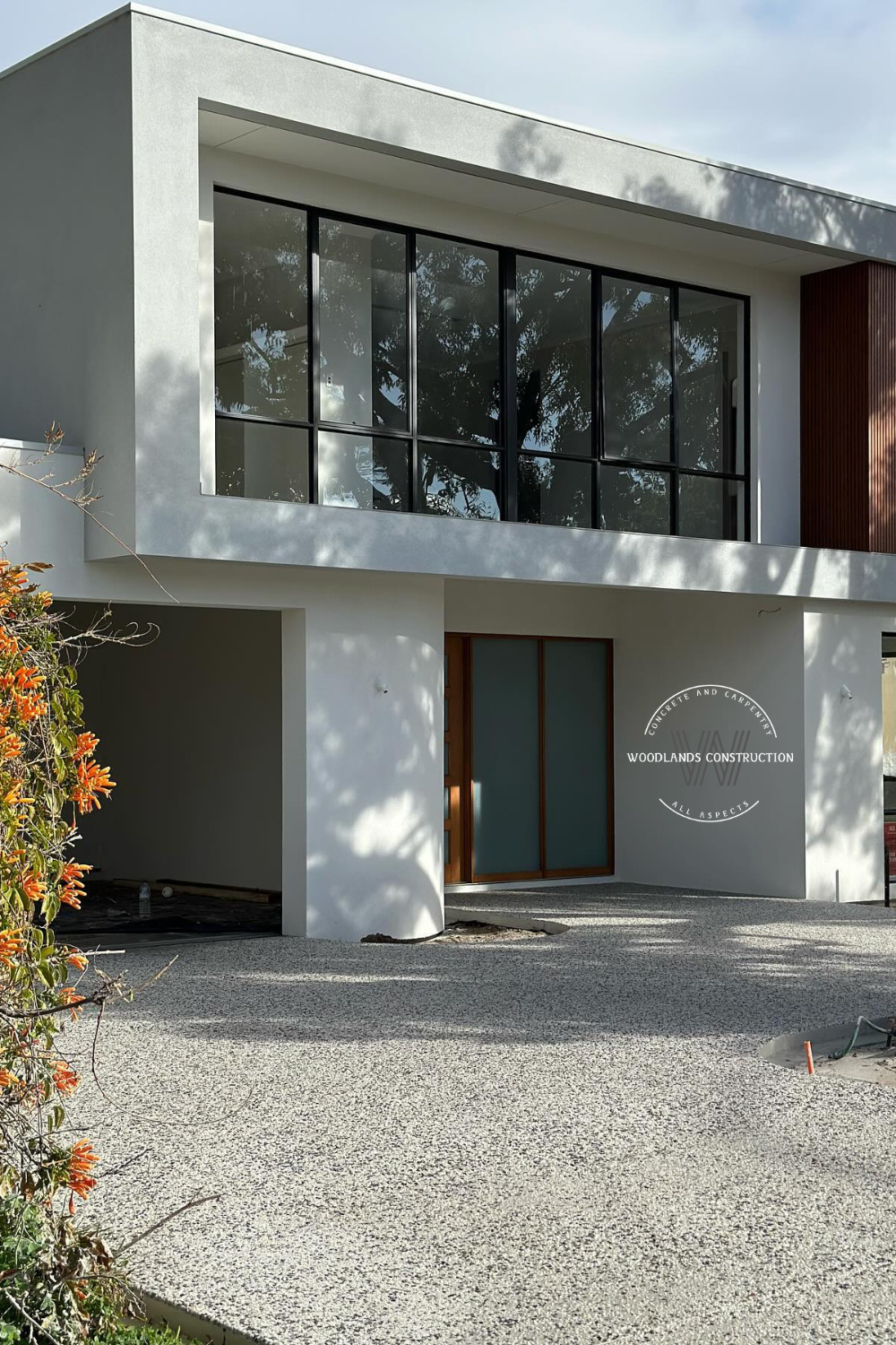 Modern gray house with large windows, exposed aggregate driveway, and orange flowers.