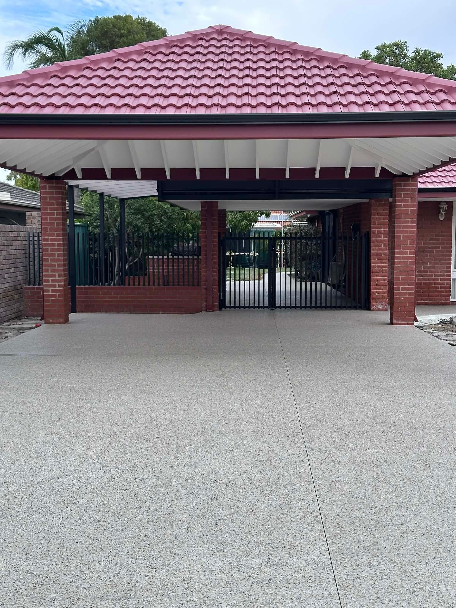 Exposed aggregate concrete driveway complimented by black fencing and red bricks.