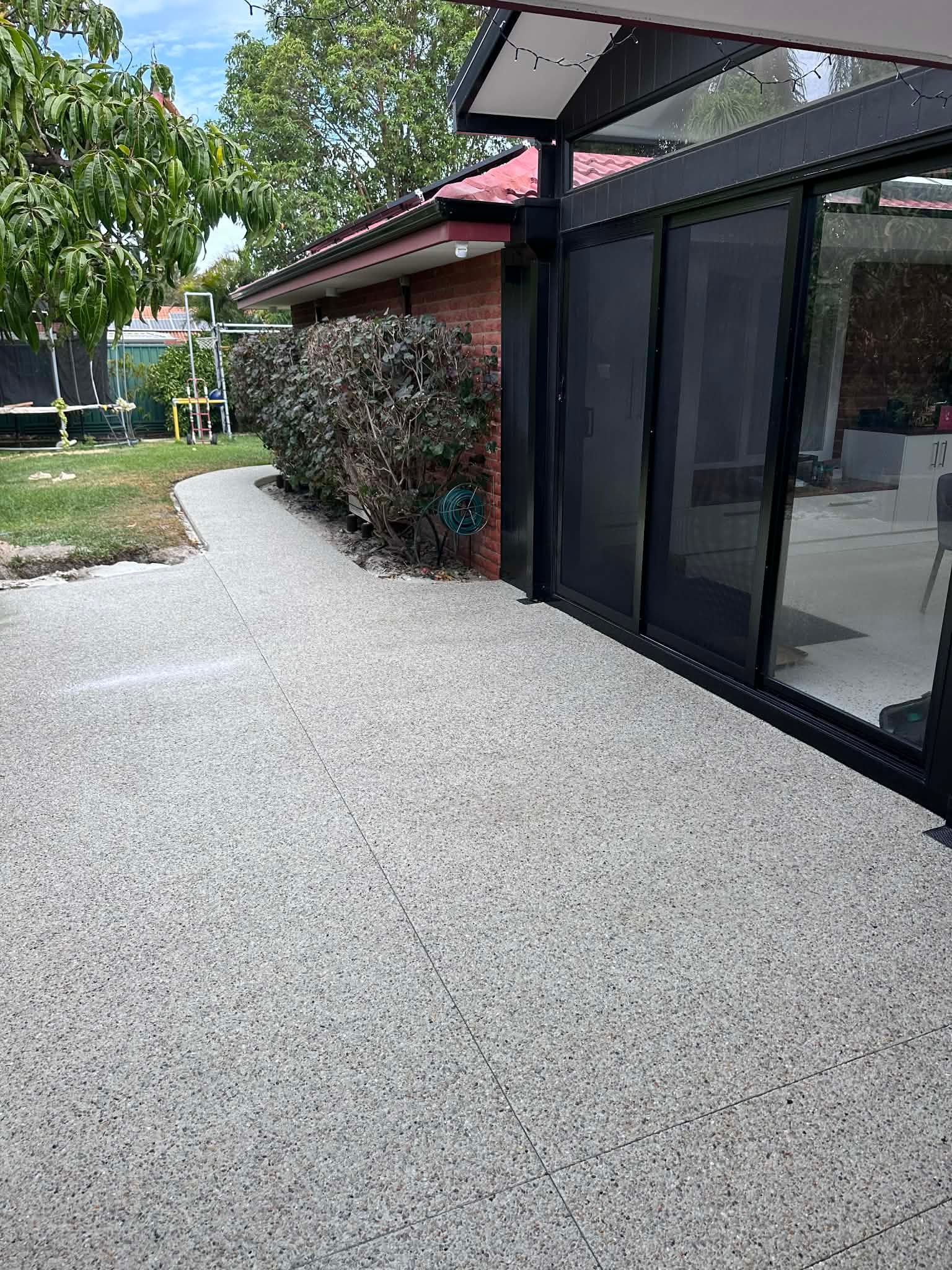 Concrete patio with bushes and a sliding glass door.