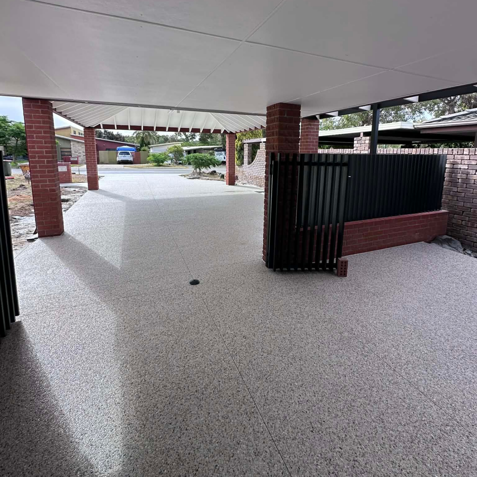 Covered patio with exposed aggregate concrete floor, brick columns, and black metal fencing.