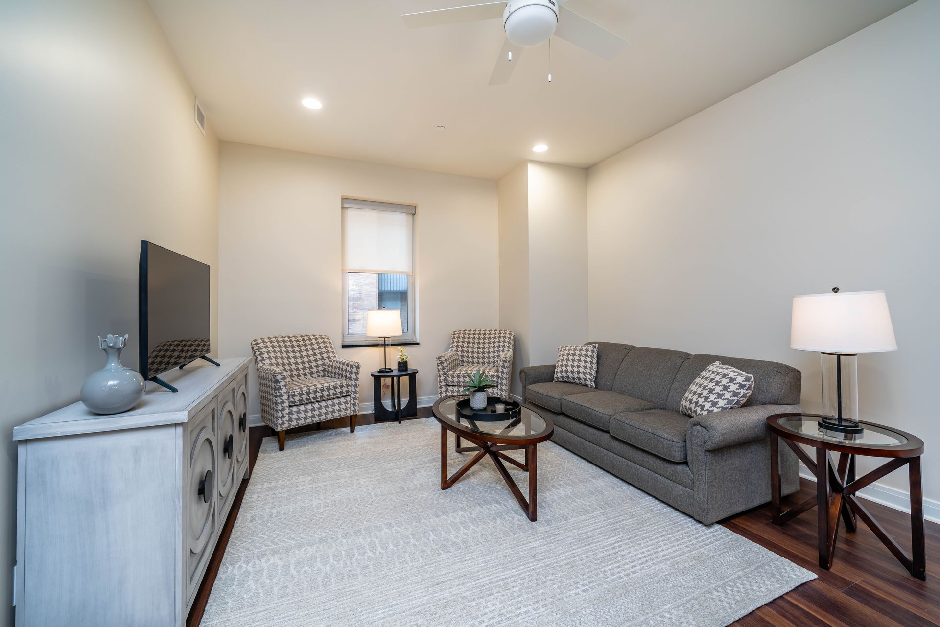 A living room with a couch , chairs , a television and a ceiling fan.