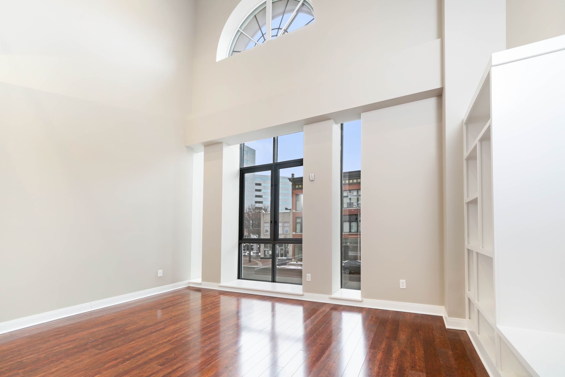 An empty living room with hardwood floors and a large window