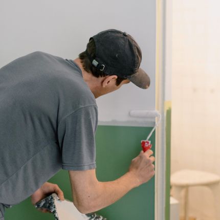 A man is painting a green wall with a roller.