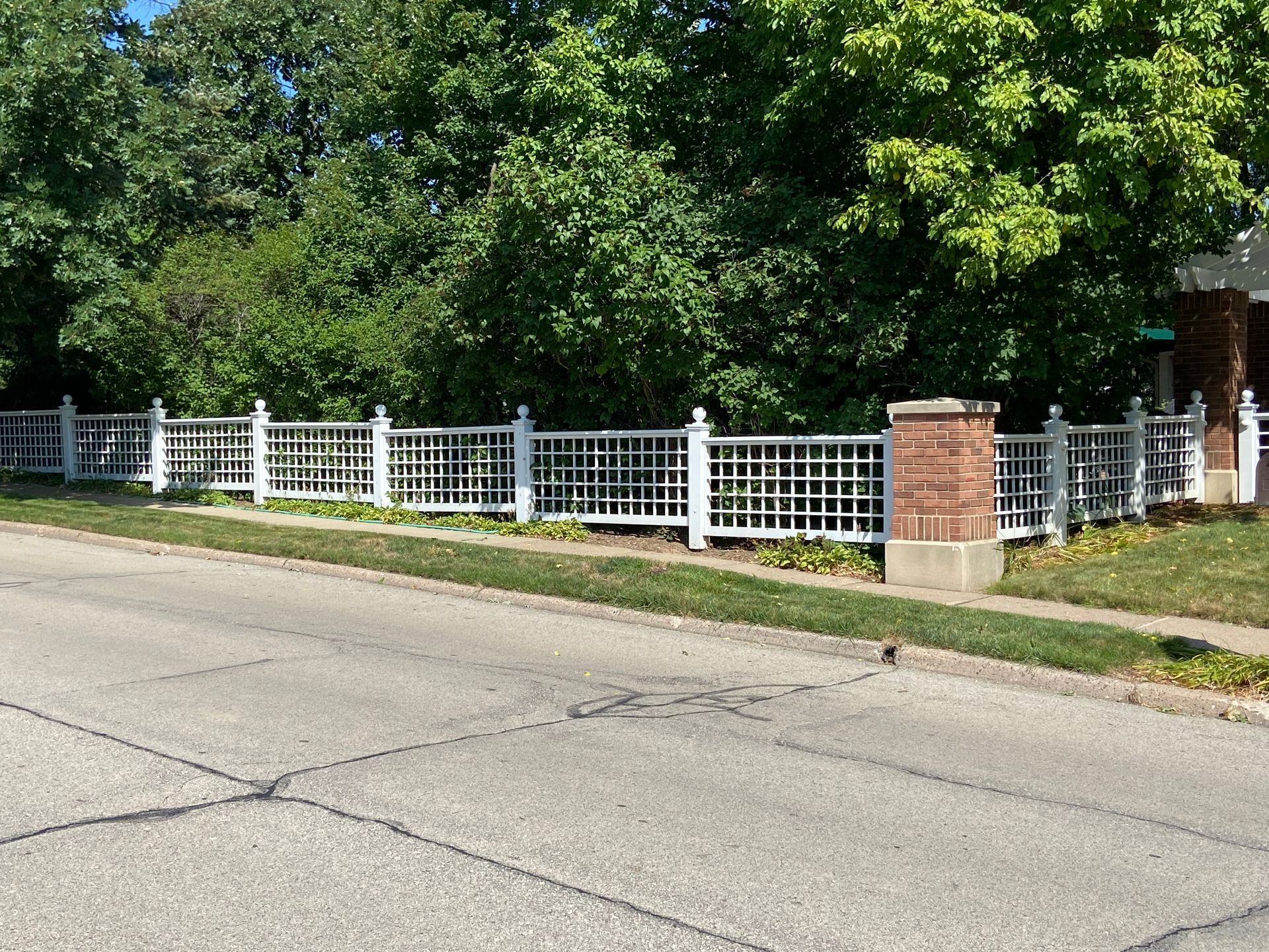A white fence surrounds a brick pillar in front of a house.