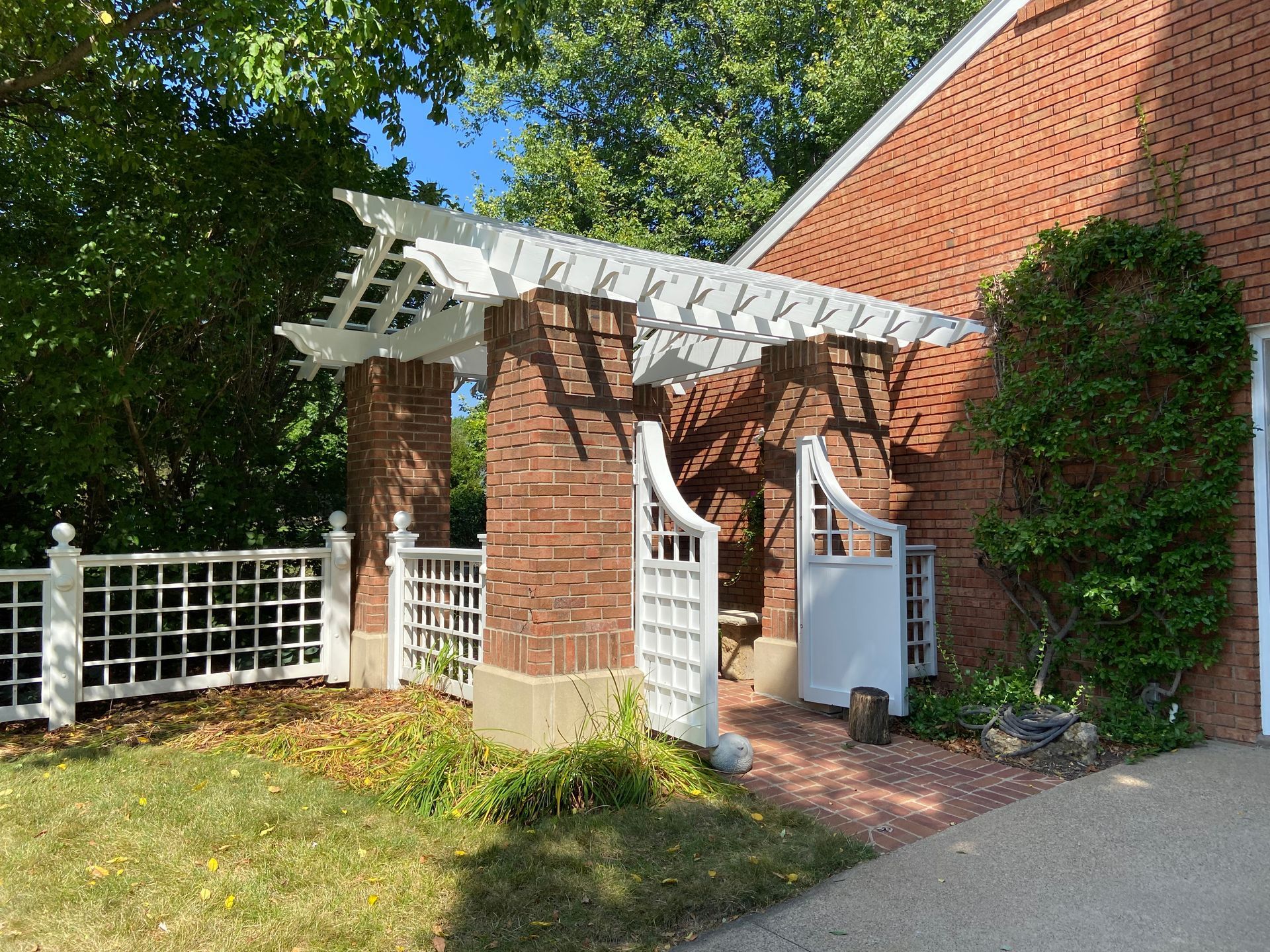 A brick house with a white pergola and a white gate.