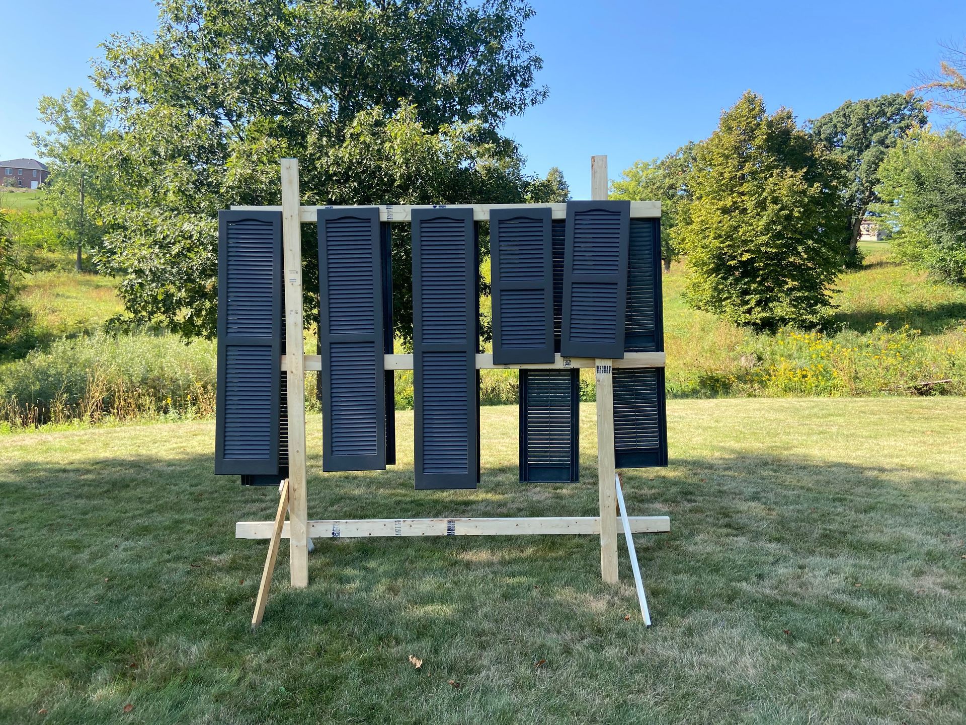 A bunch of black shutters are hanging on a wooden rack in a field.