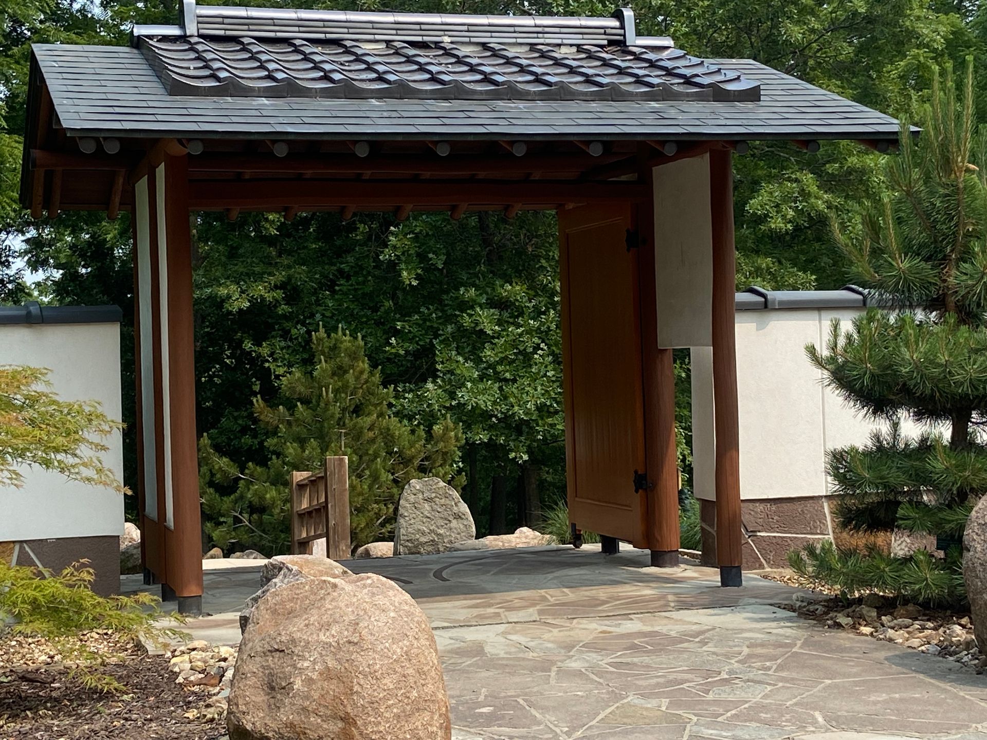 A wooden gate with a slate roof is surrounded by rocks and trees