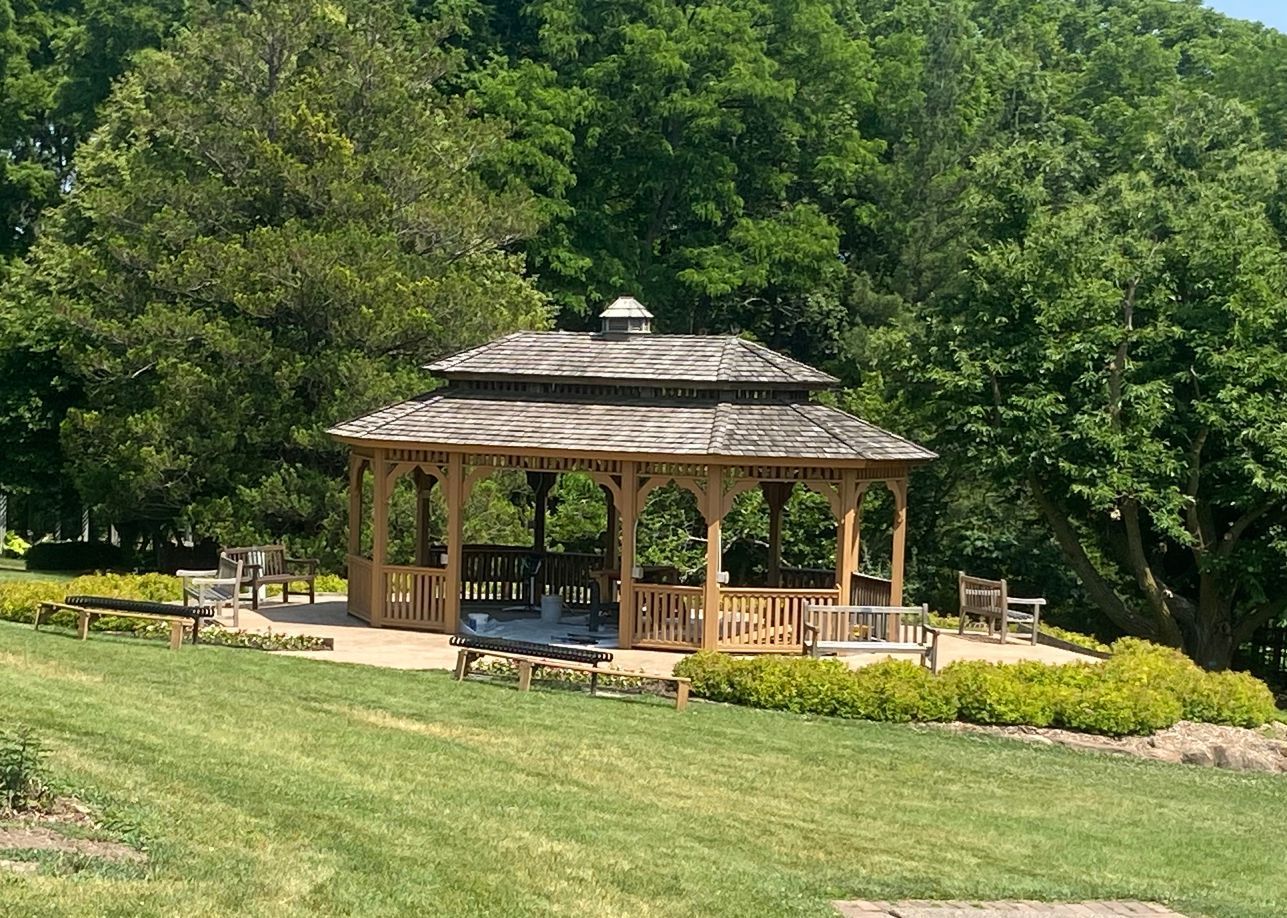 A gazebo is sitting in the middle of a lush green field surrounded by trees.