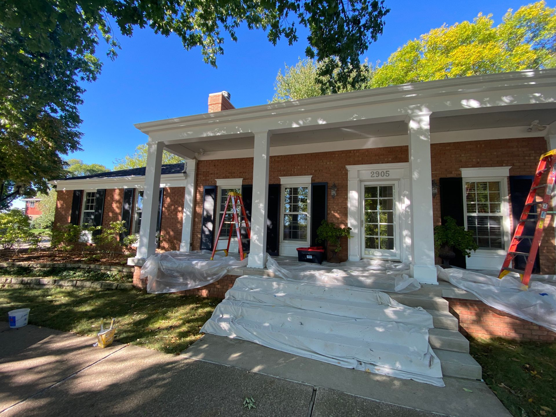 A brick house with a large porch is being painted white.