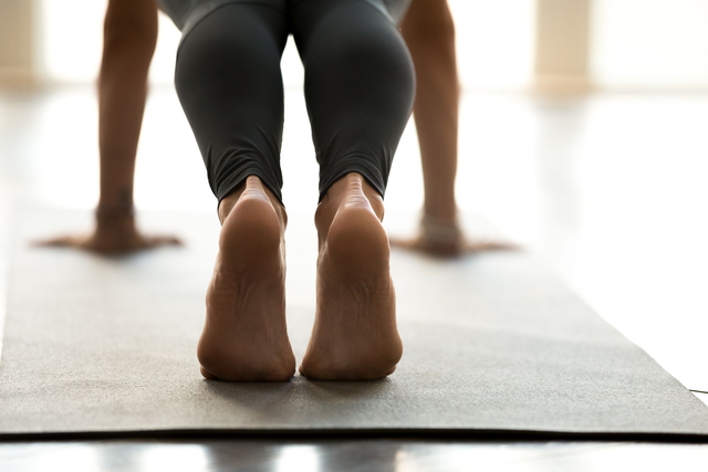Person doing yoga on a mat, feet visible, with gray leggings, arms extended.
