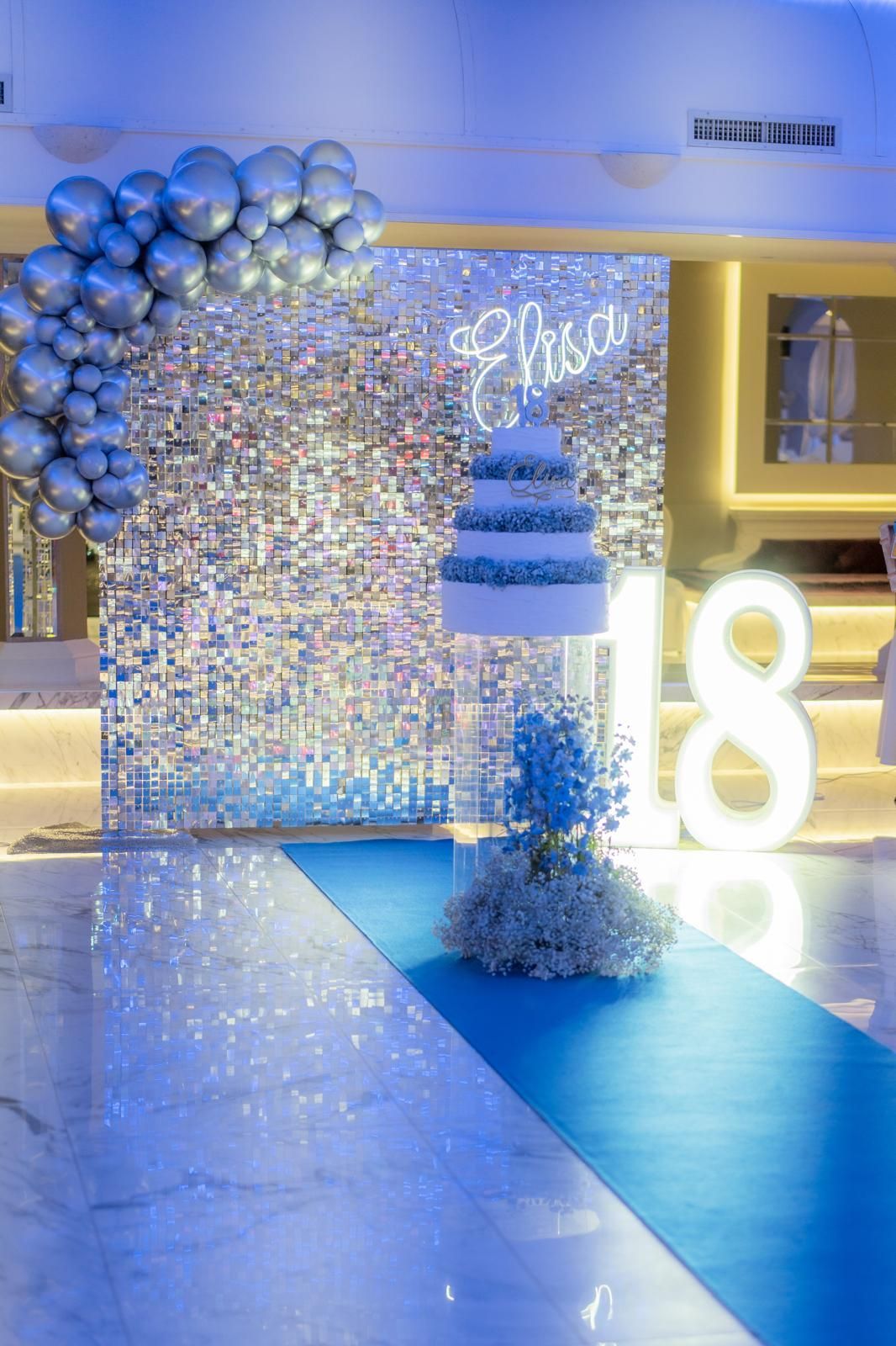 C'è una torta su un supporto davanti a una parete con dei palloncini.