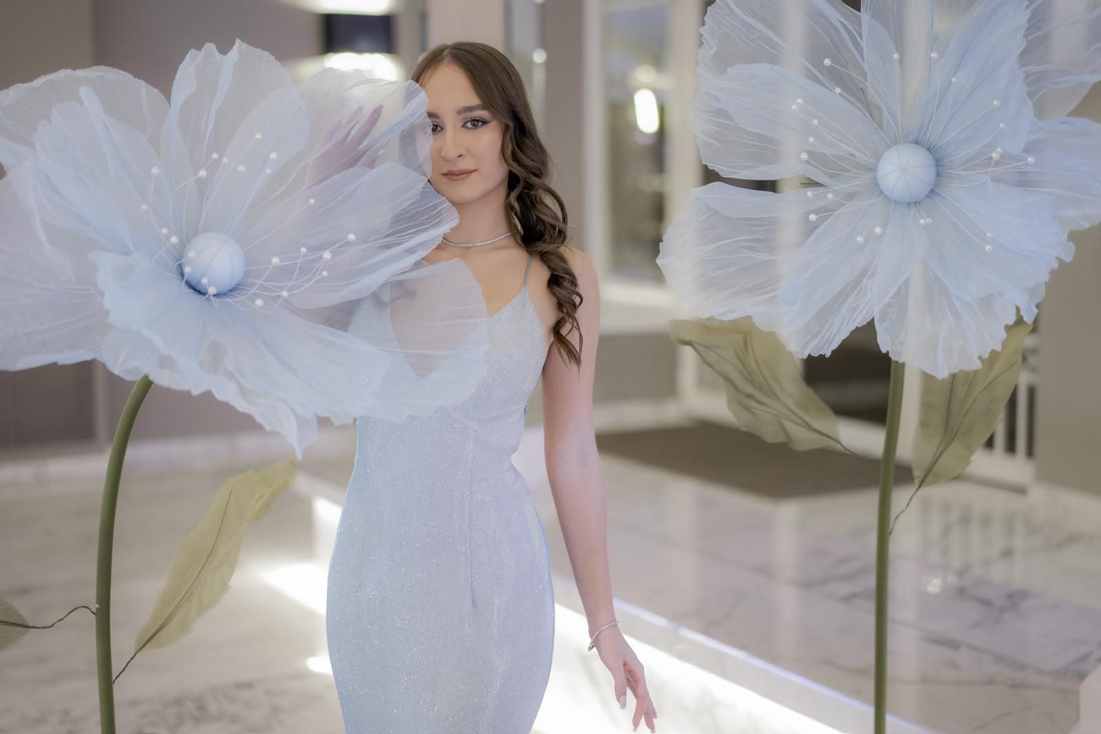 Una donna vestita di bianco è in piedi davanti a dei fiori giganti.