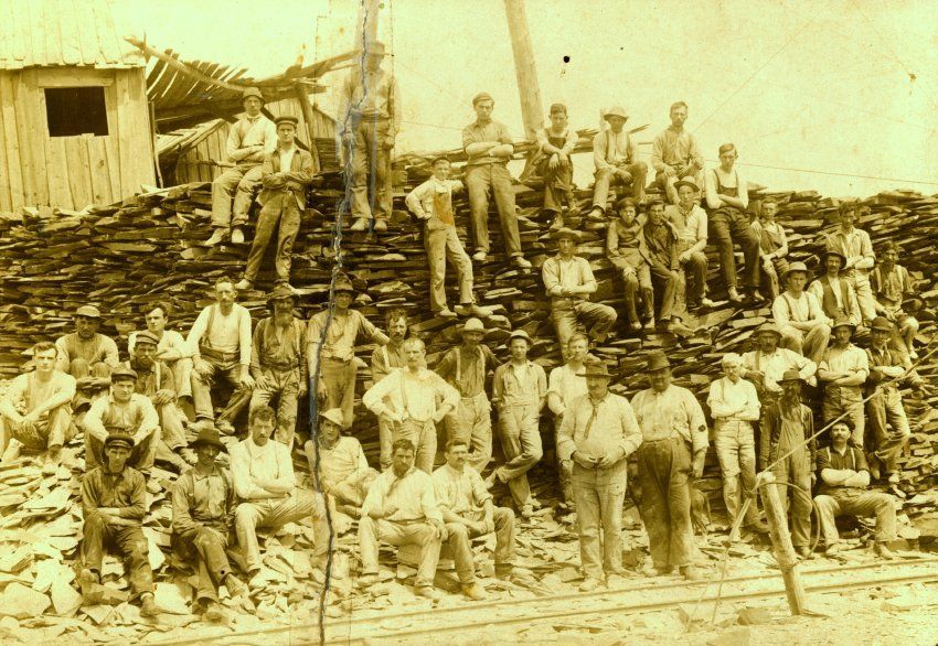 Men and boys stand in front of a shanty on a small pile of slag