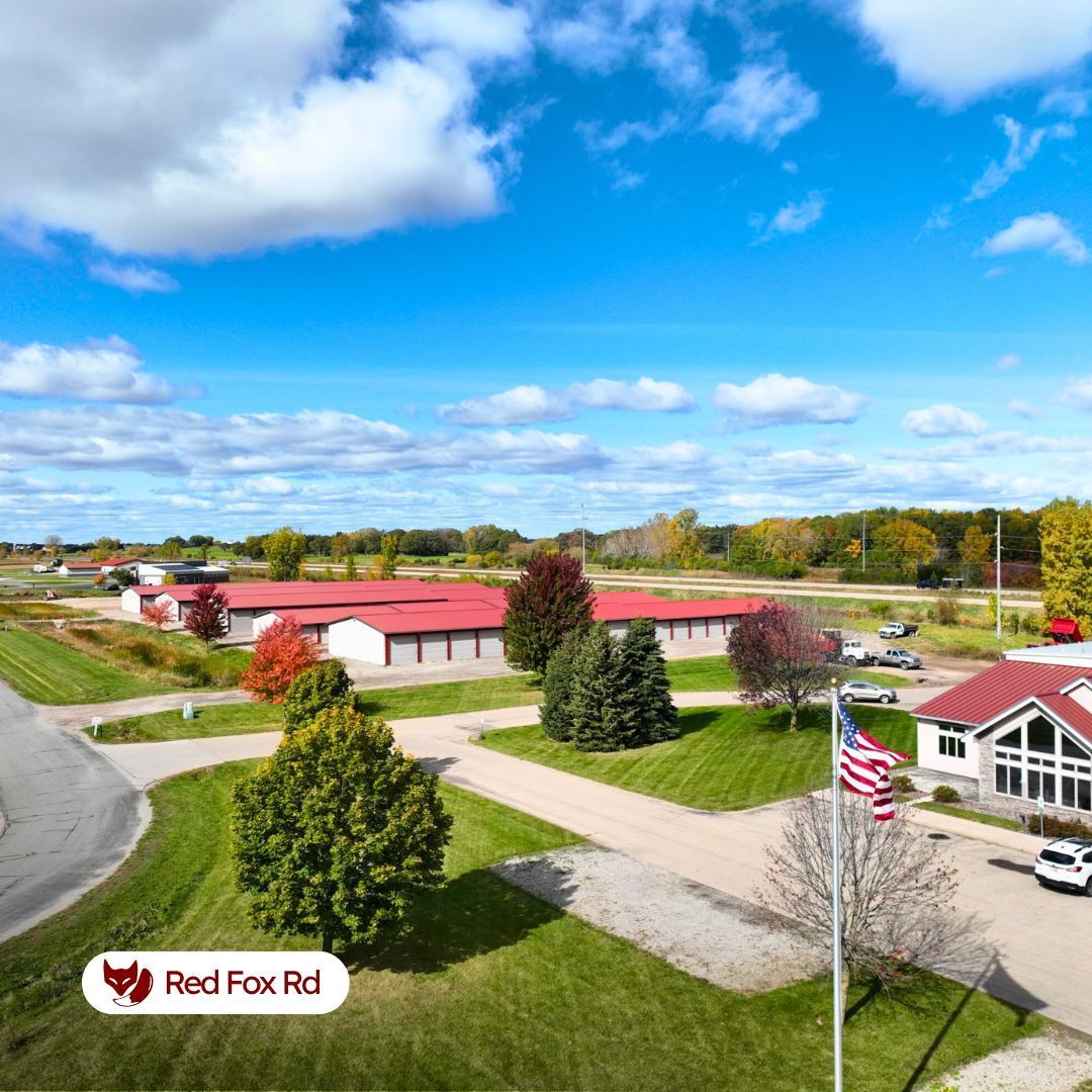 Oshkosh Storage units with red roofs and white buildings. Green lawn, blue sky, and an American flag.