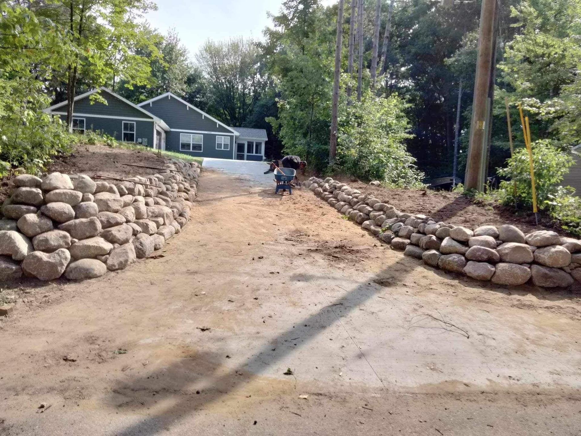 A man is pushing a wheelbarrow down a dirt road next to a house.