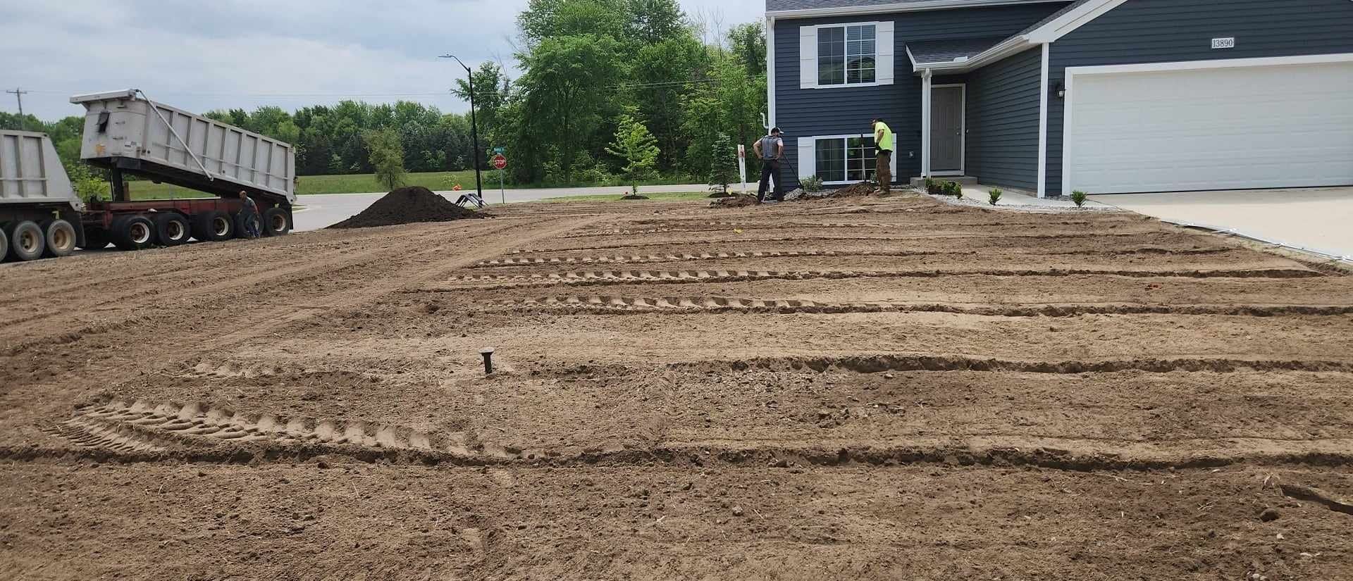 A dump truck is loading dirt into a driveway in front of a house.
