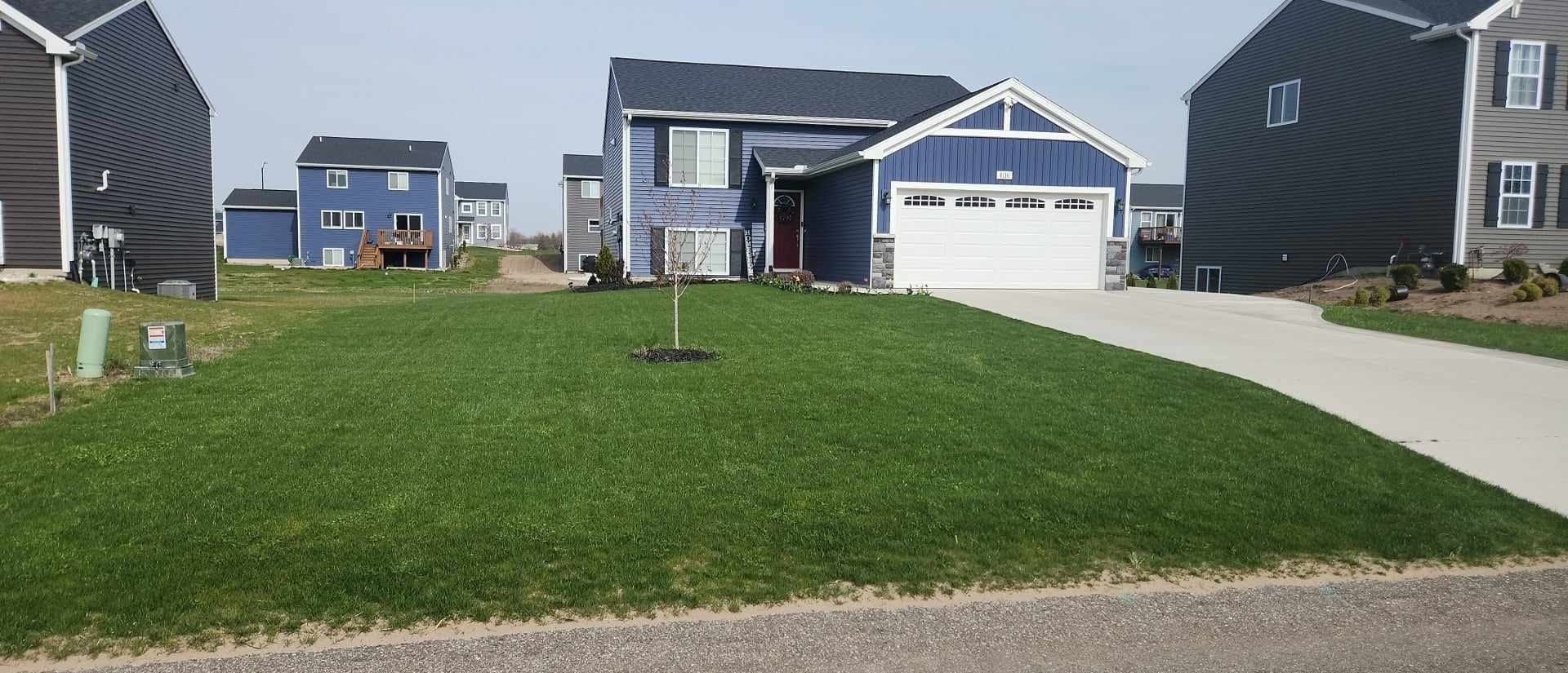 A blue house with a white garage door is surrounded by other houses in a residential area.