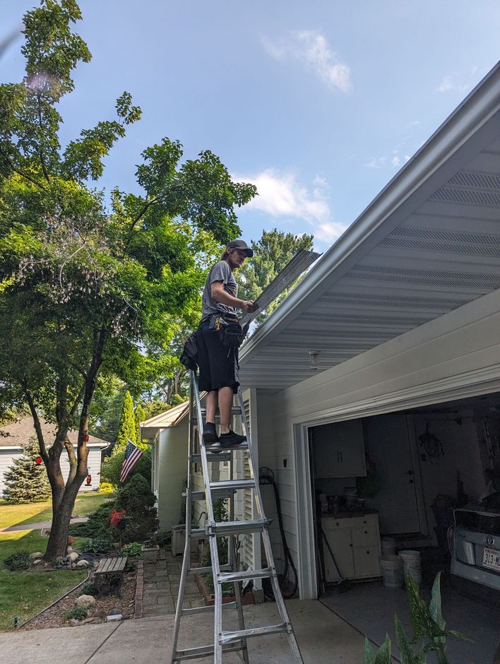 A man is standing on a ladder working on the roof of a house.