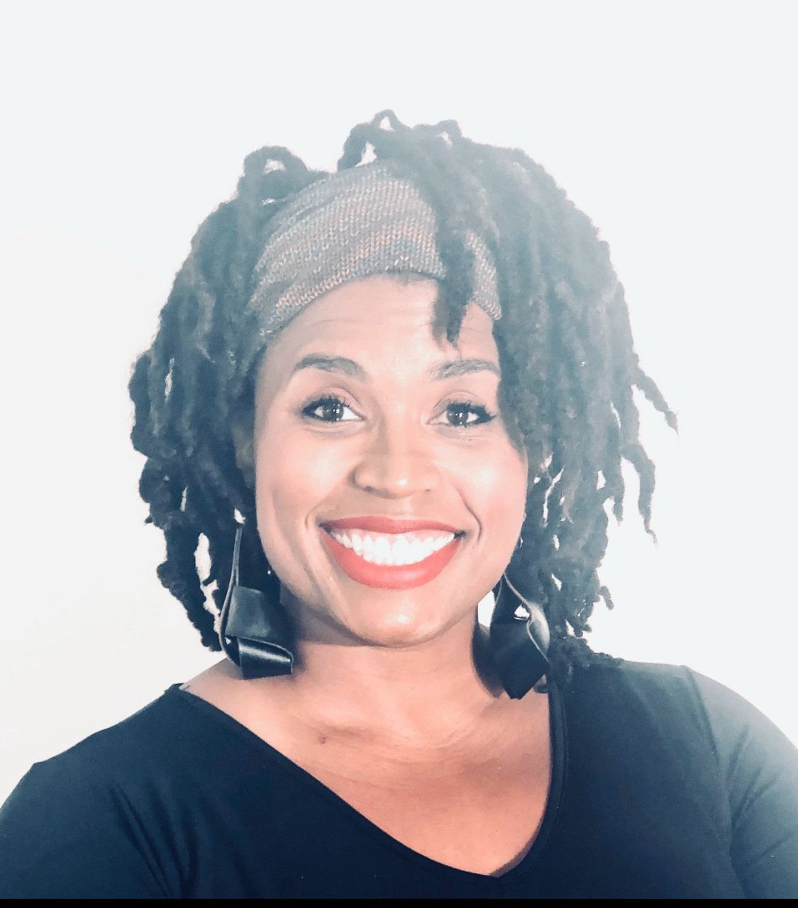A smiling Black man in a white shirt with a chain. He's looking at the camera.
