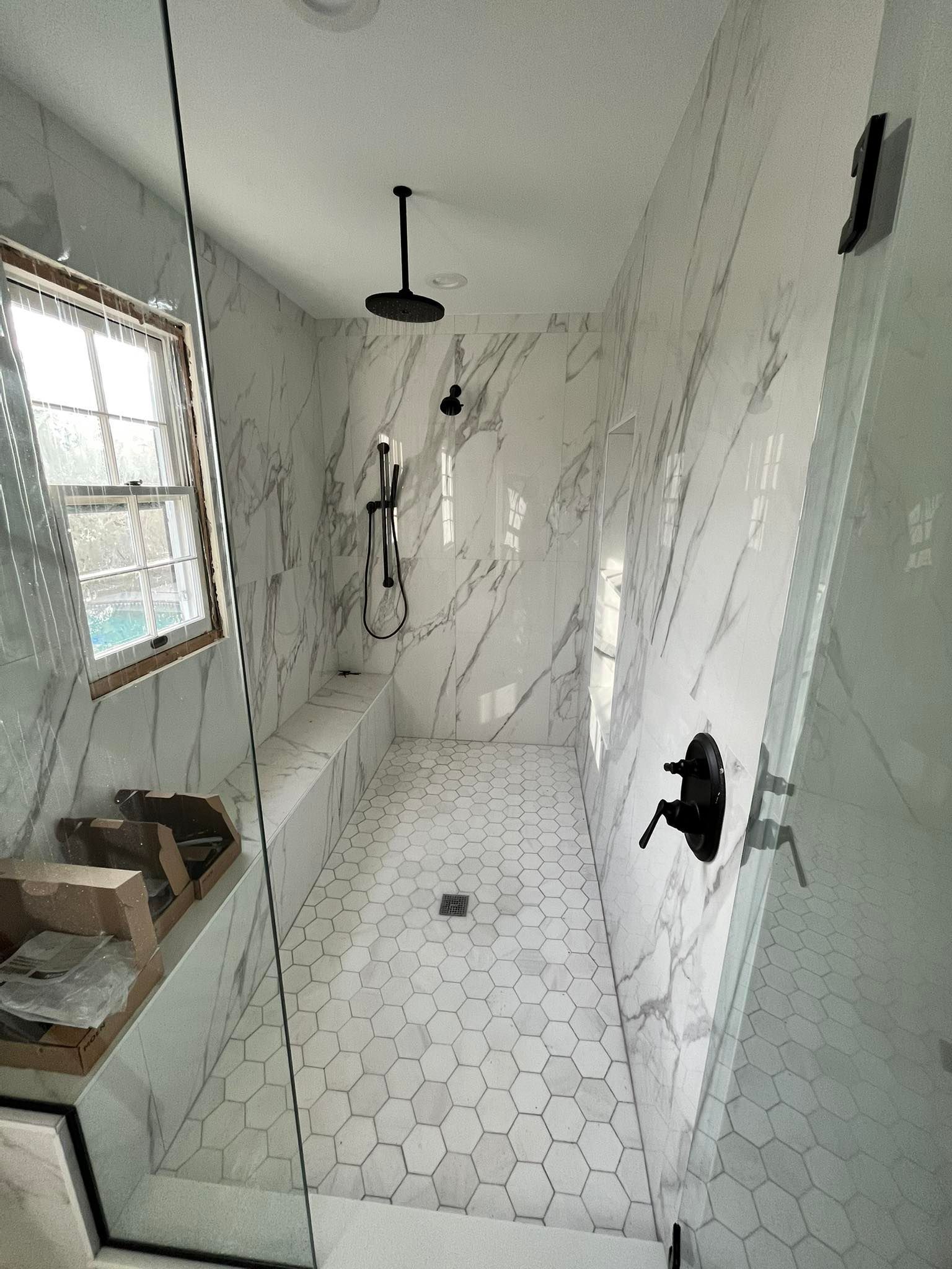 A modern walk-in shower with white marble walls, a hexagon tile floor, black fixtures, and a built-in bench.