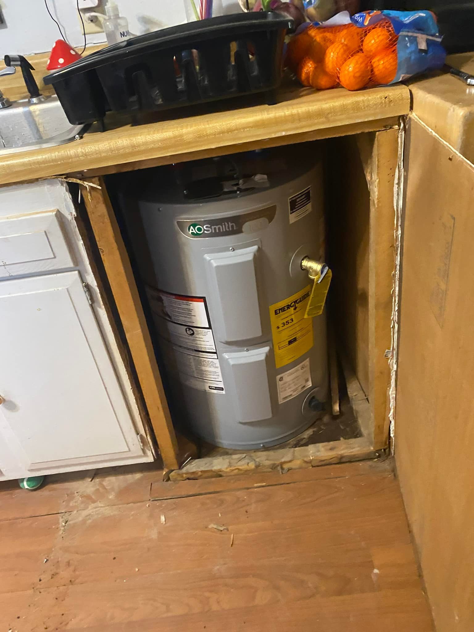 A grey electric water heater installed in an open kitchen cabinet space under a countertop.