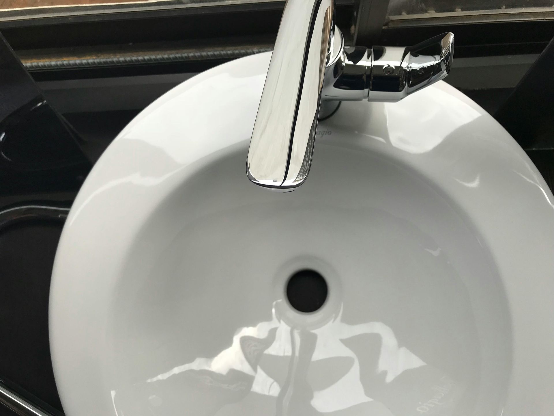 A white, circular bathroom sink with a silver faucet, viewed from directly above.