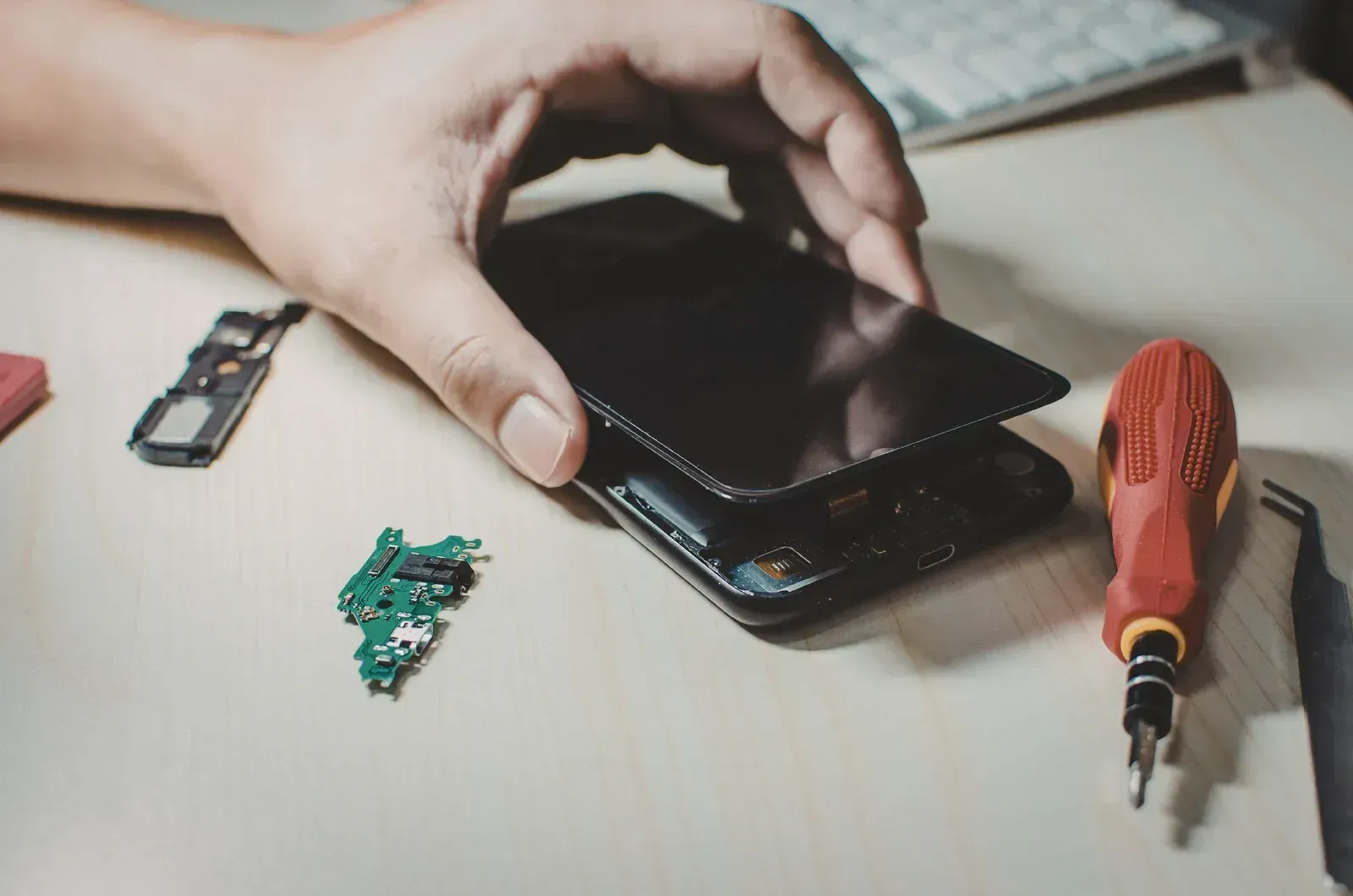 Hand using a smartphone on a desk beside a screwdriver and small electronic parts
