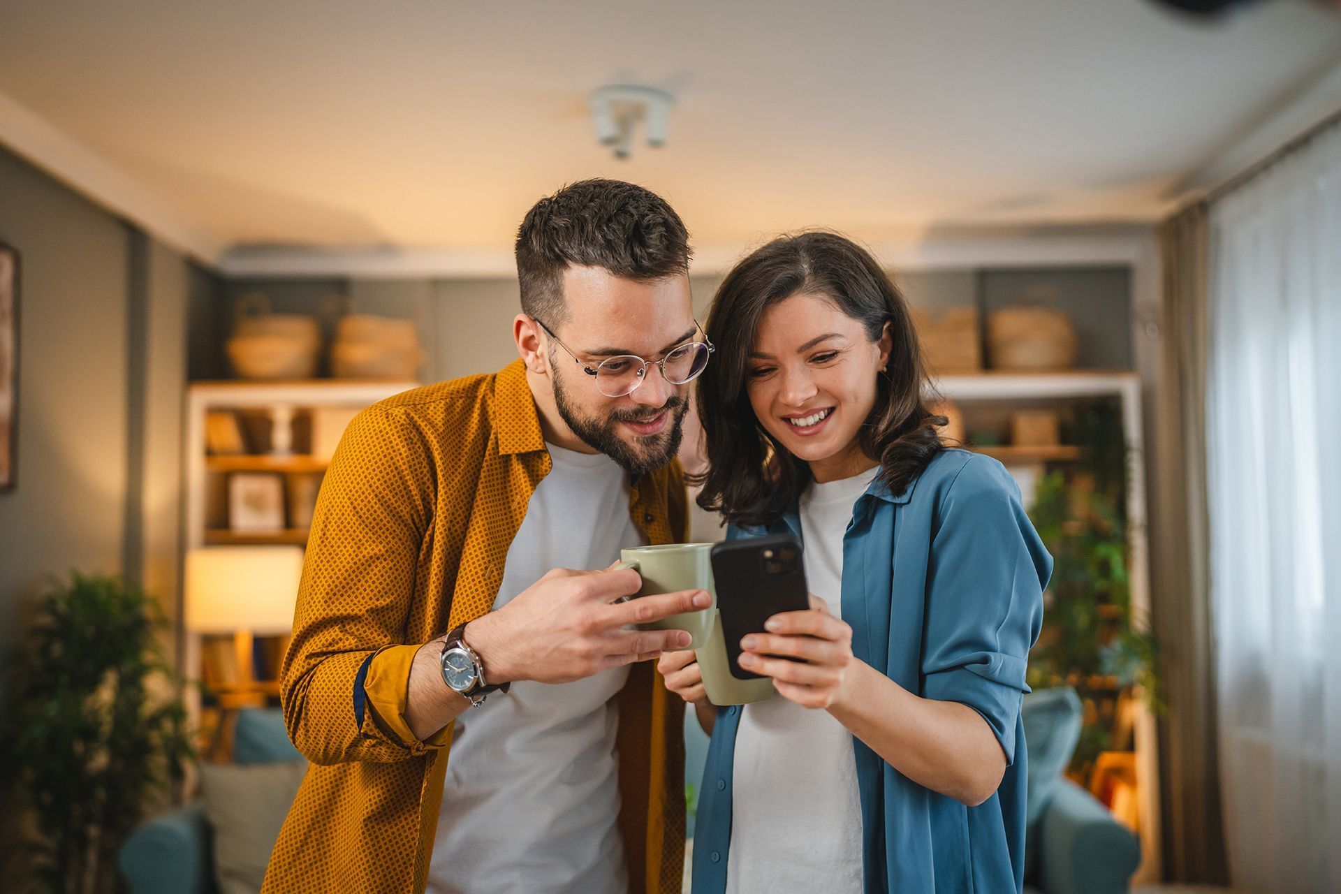 A man and a woman are looking at a cell phone together in a living room.