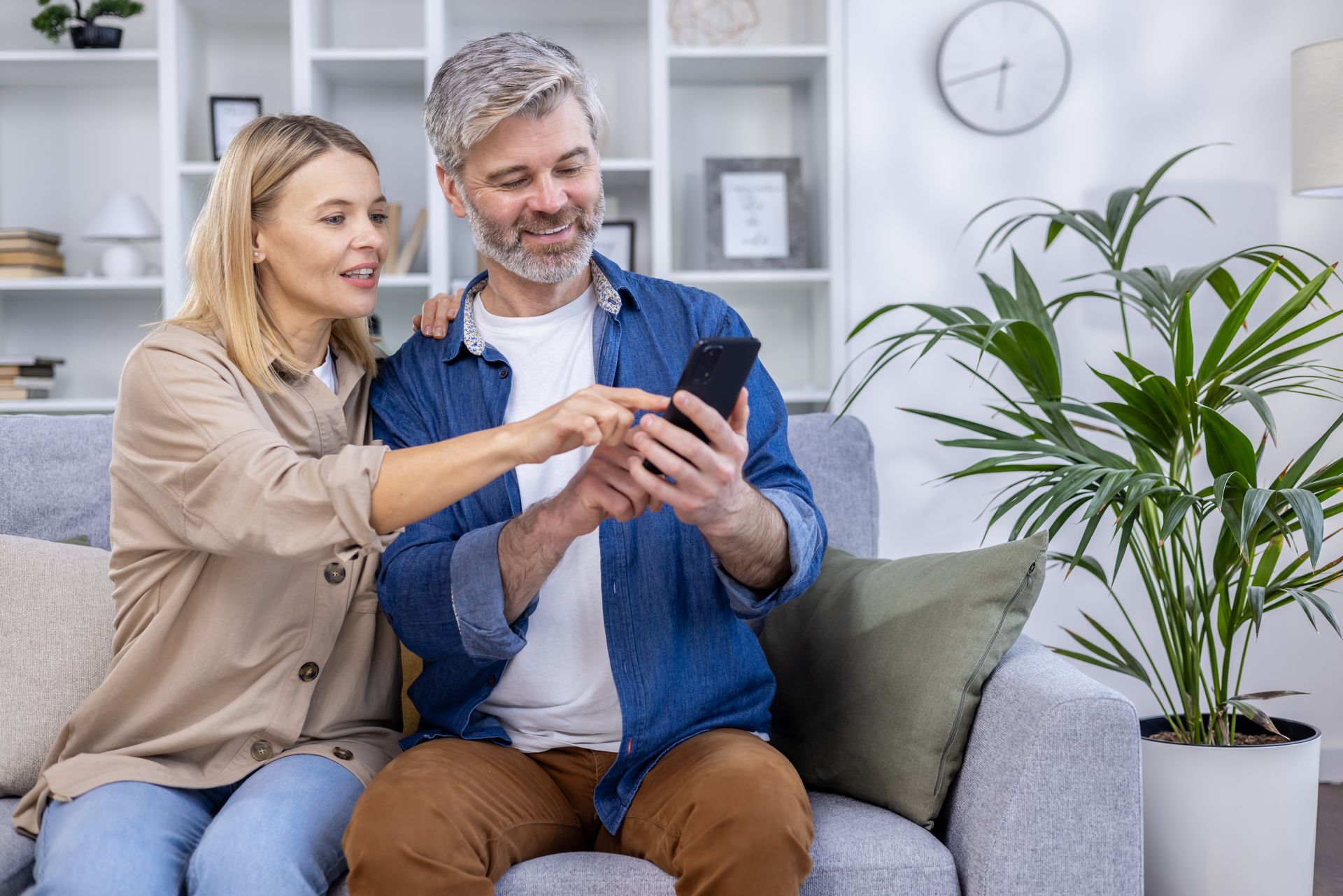 A man and a woman are sitting on a couch looking at a cell phone.