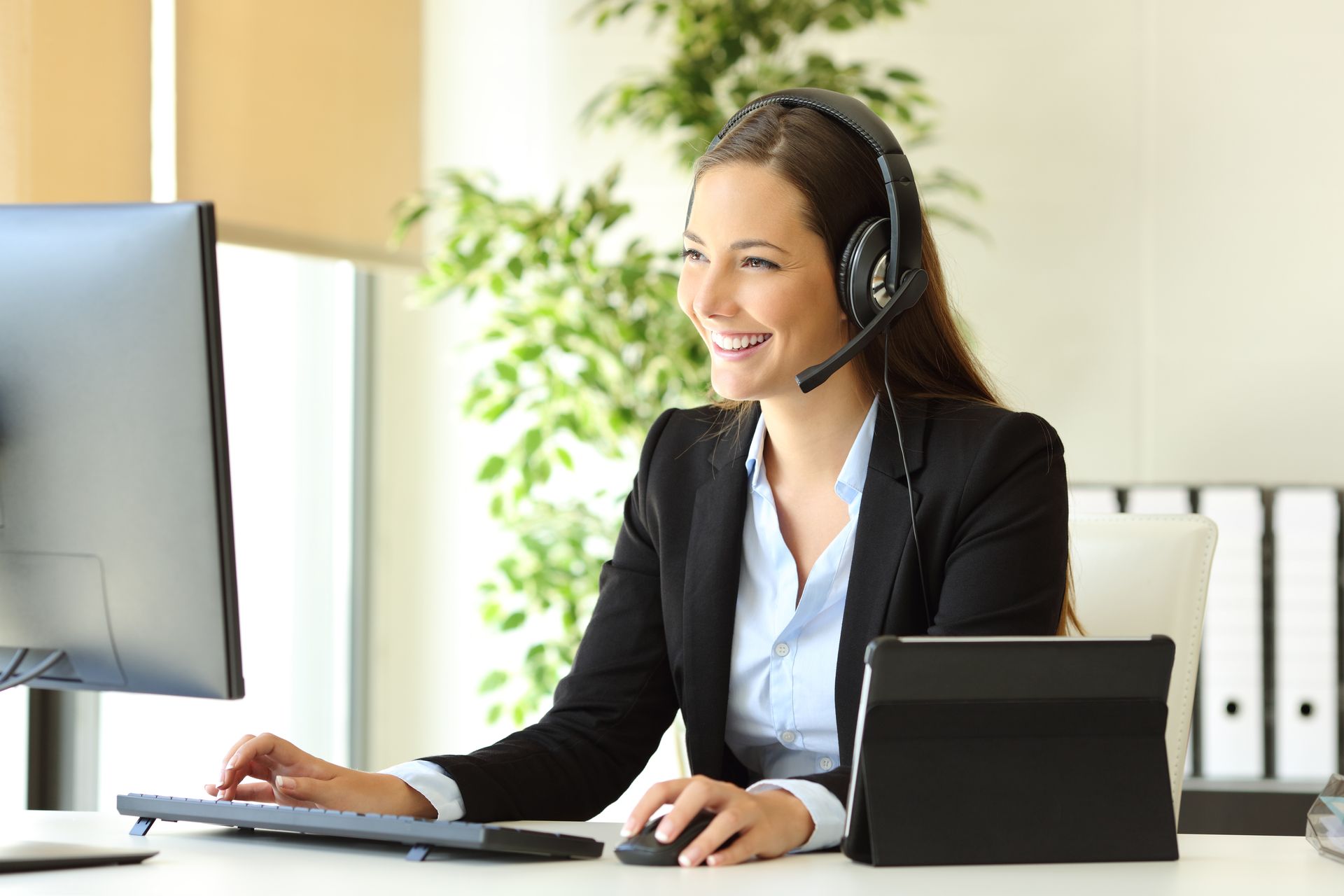A woman wearing a headset is sitting at a desk in front of a computer.