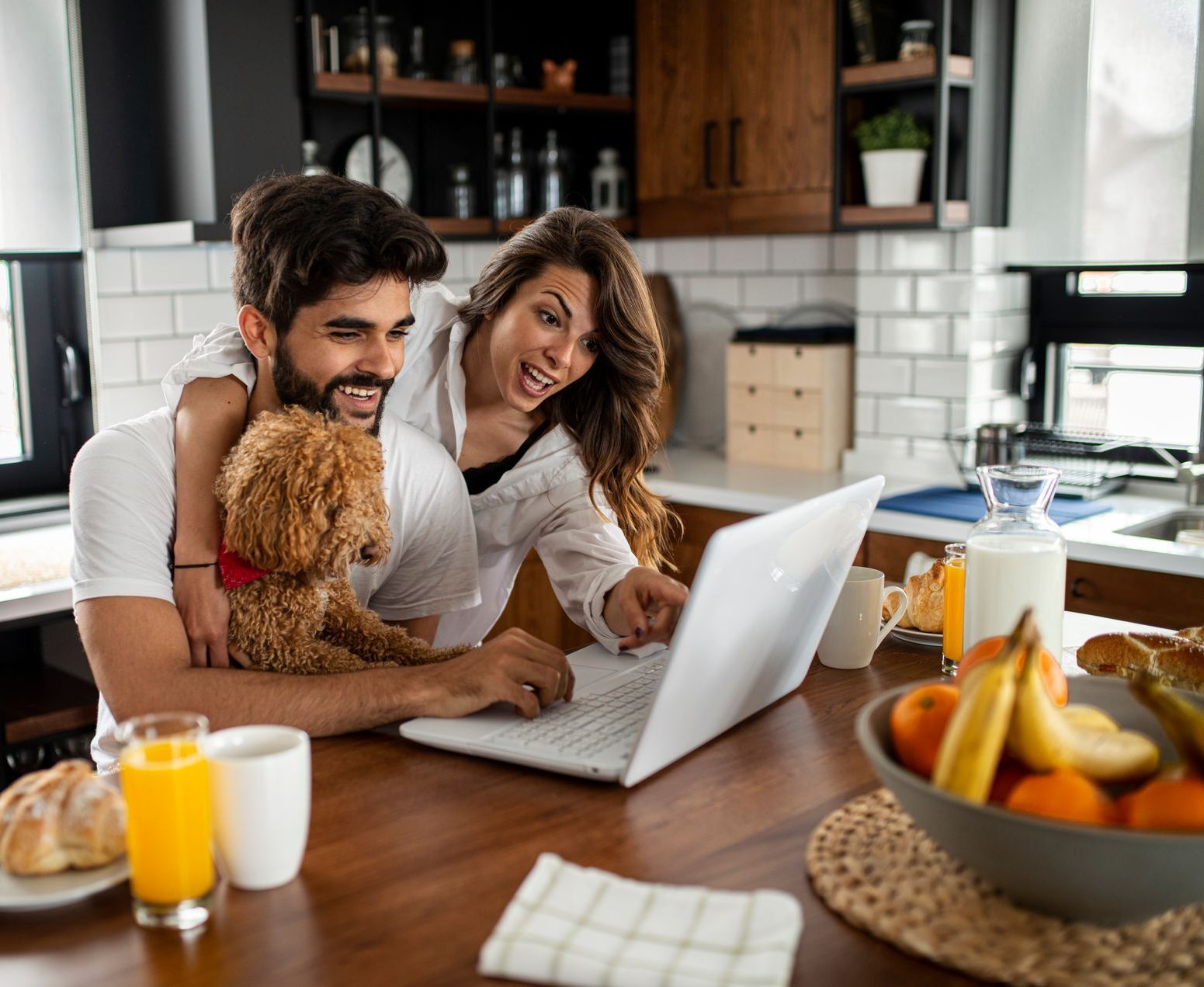 A man and woman are sitting at a table with a dog and a laptop.