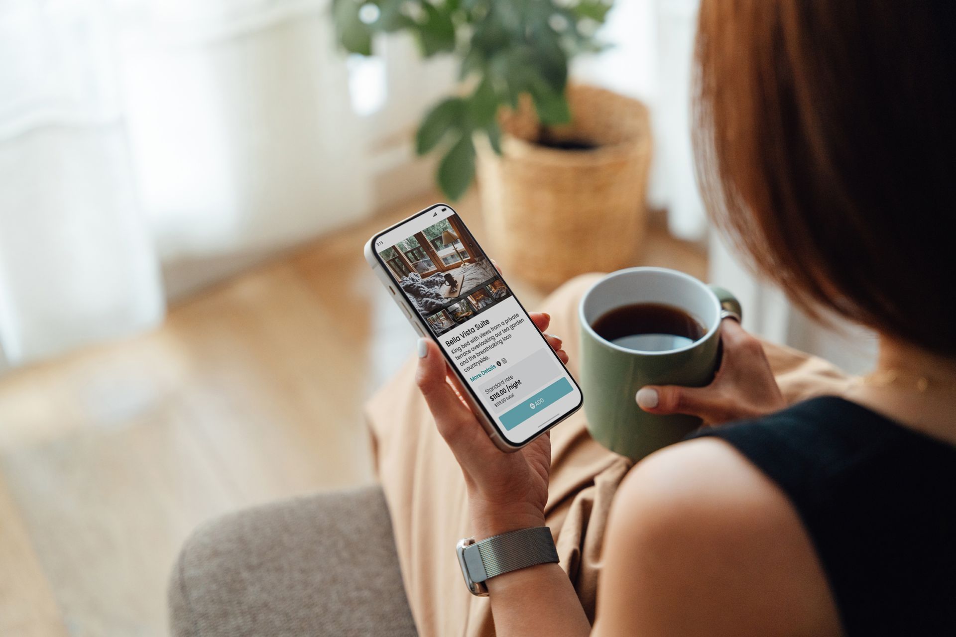 A woman is sitting on a couch holding a cup of coffee and looking at her phone.
