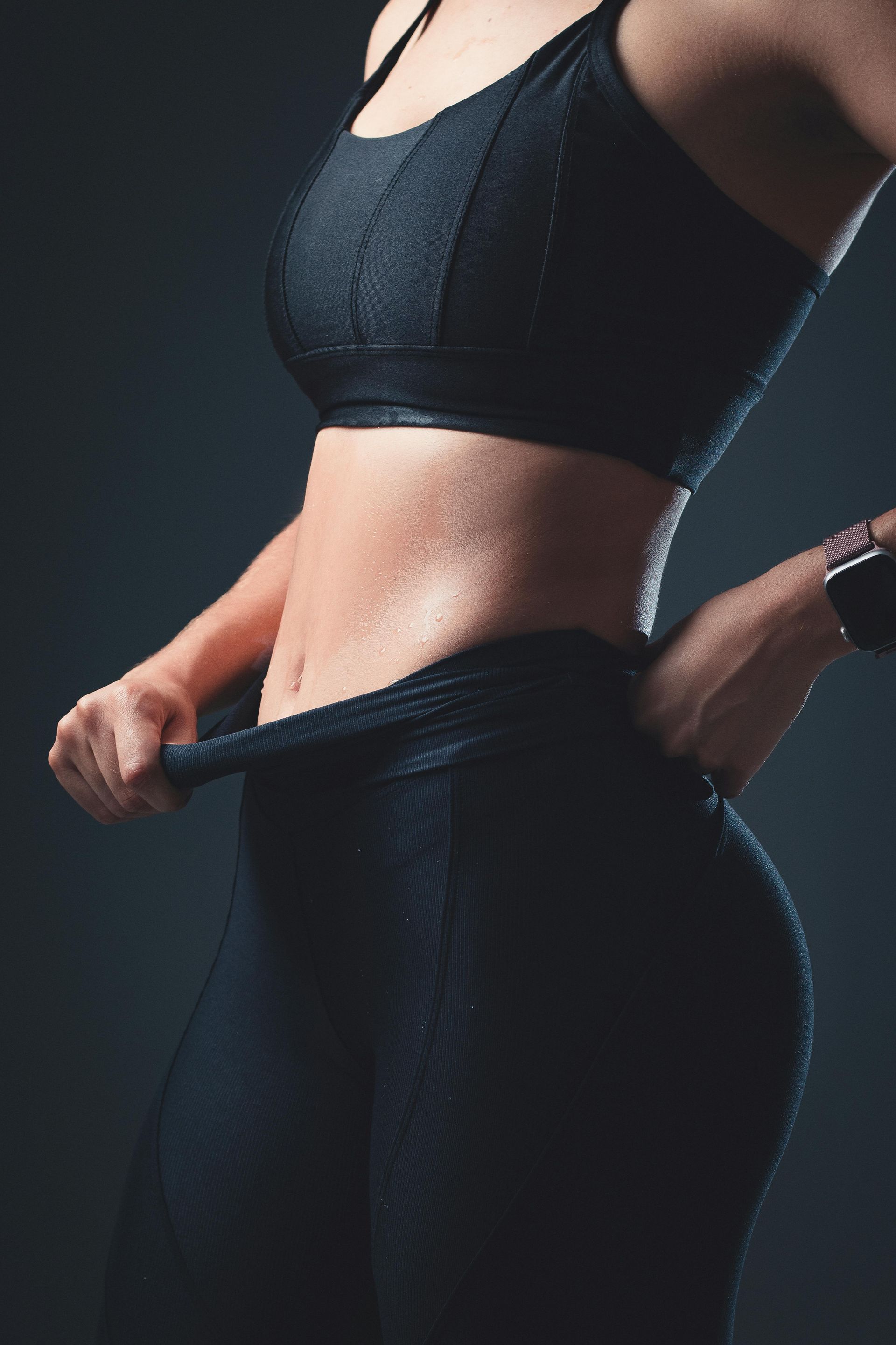 Mujer vestida con ropa deportiva negra levantándose los leggings, resaltando un abdomen tonificado.