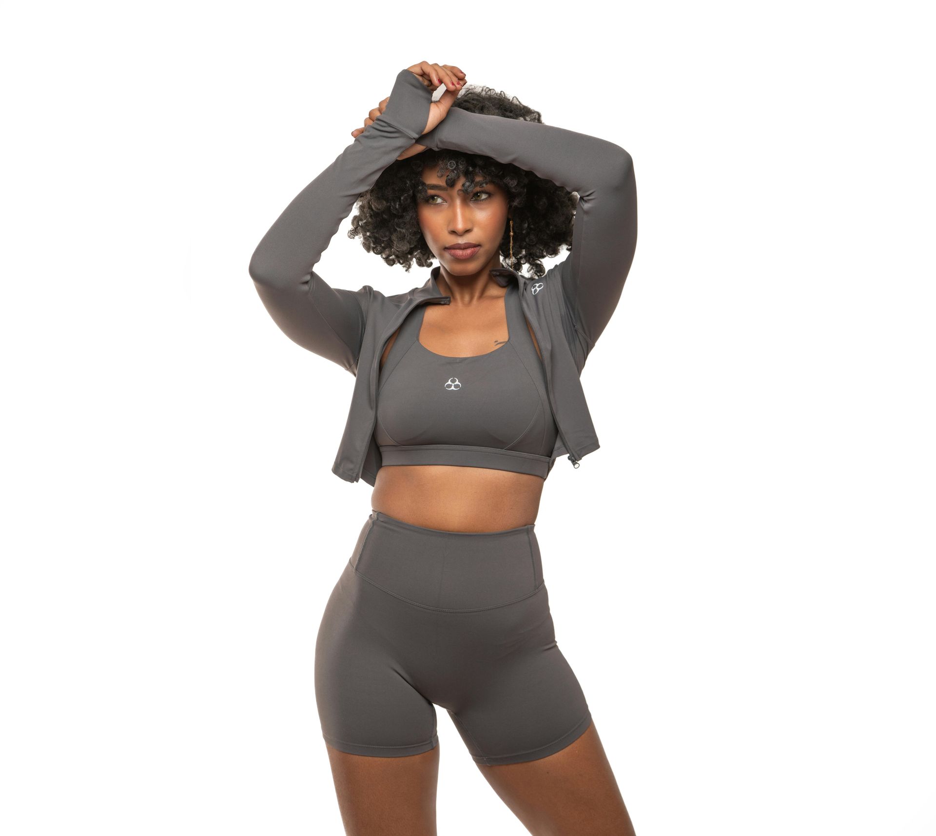 Mujer con conjunto deportivo gris, brazos levantados y mirada hacia otro lado.