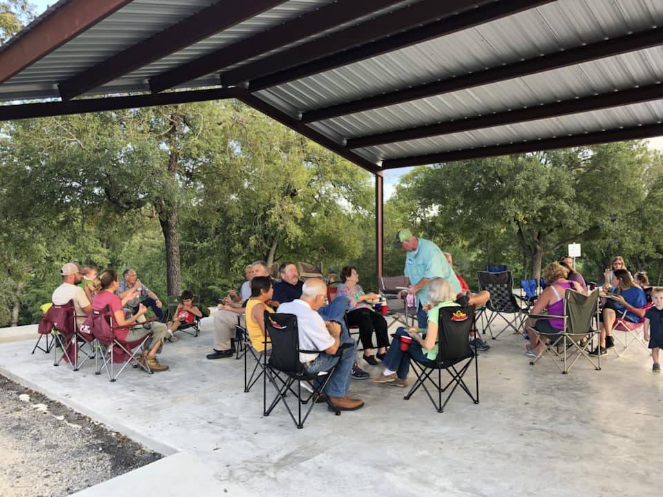 A group of people are sitting in a circle under a covered area.