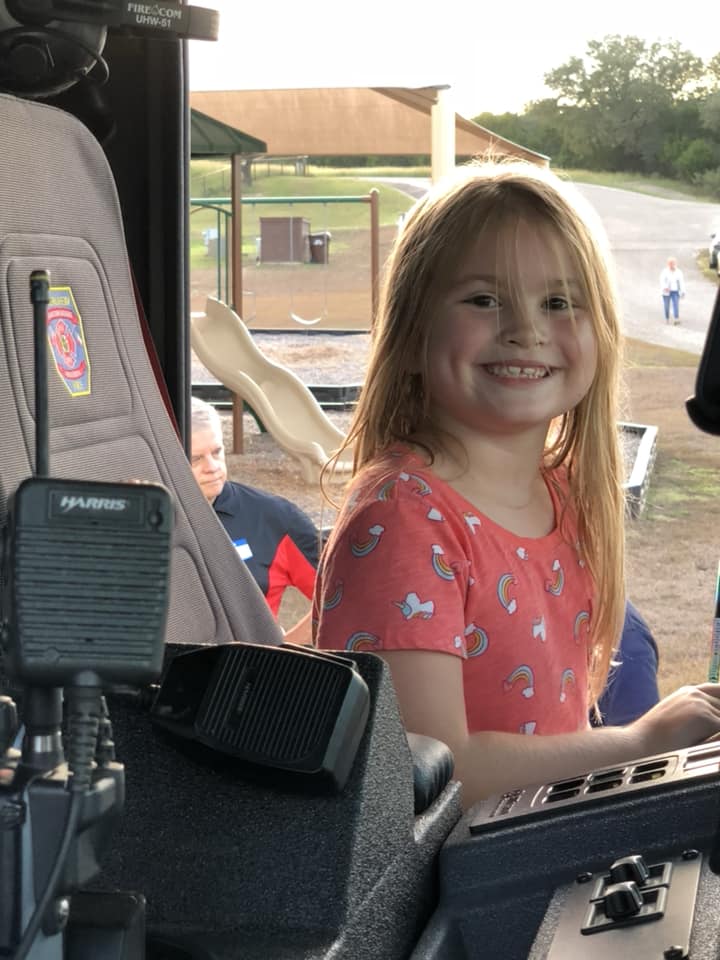 A little girl is sitting in the driver 's seat of a fire truck