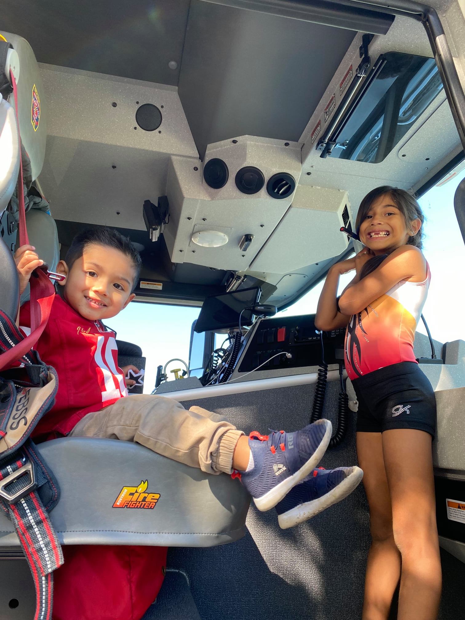 A boy and a girl are sitting in the front of a fire truck.